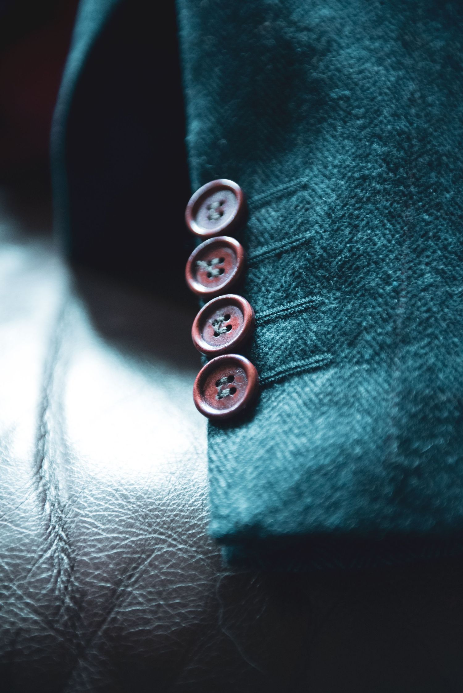 Close-up of dark teal suit jacket buttons showing detailed stitching.