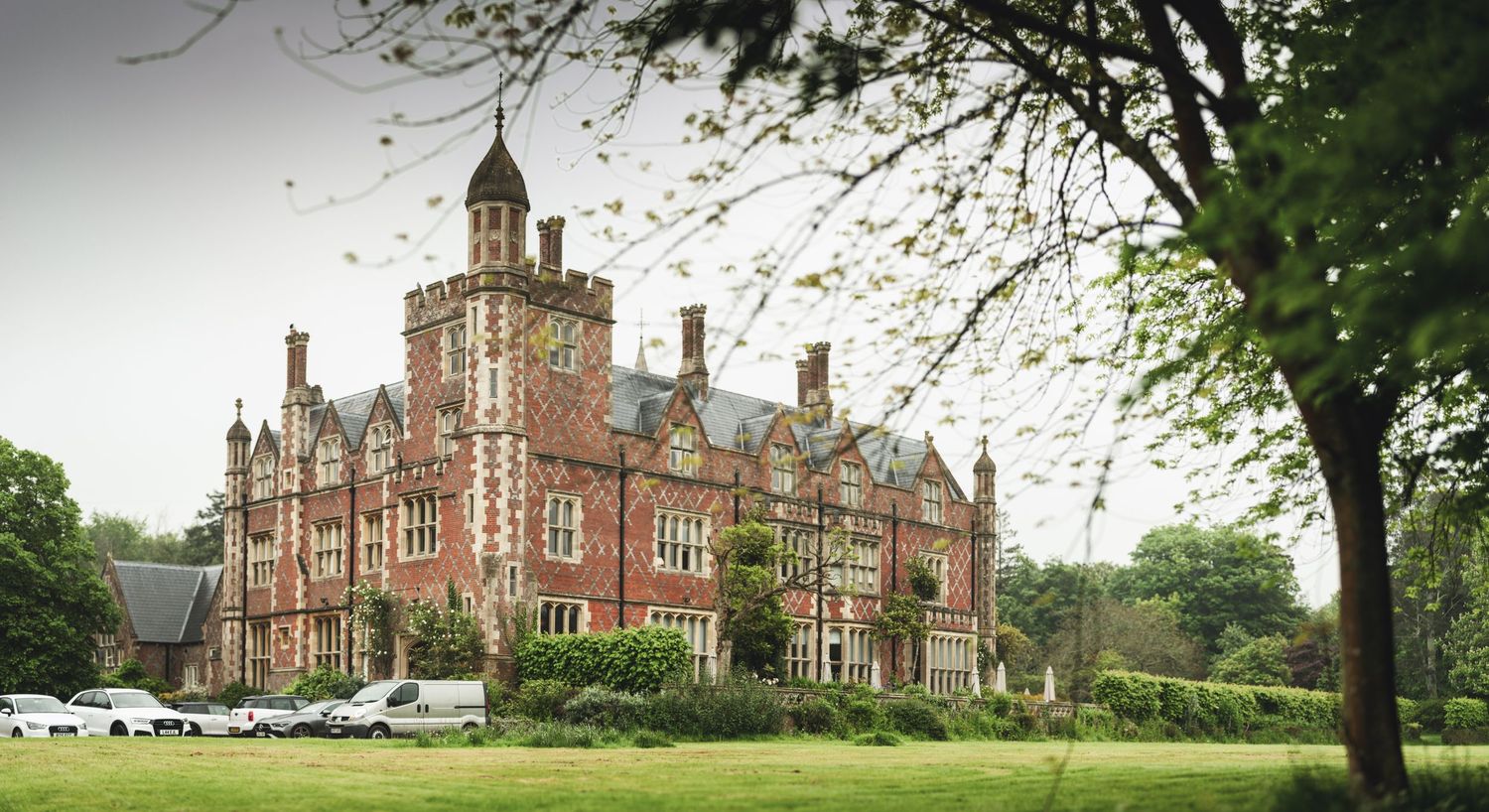Majestic red brick Victorian mansion with tower and ornate architecture surrounded by trees.