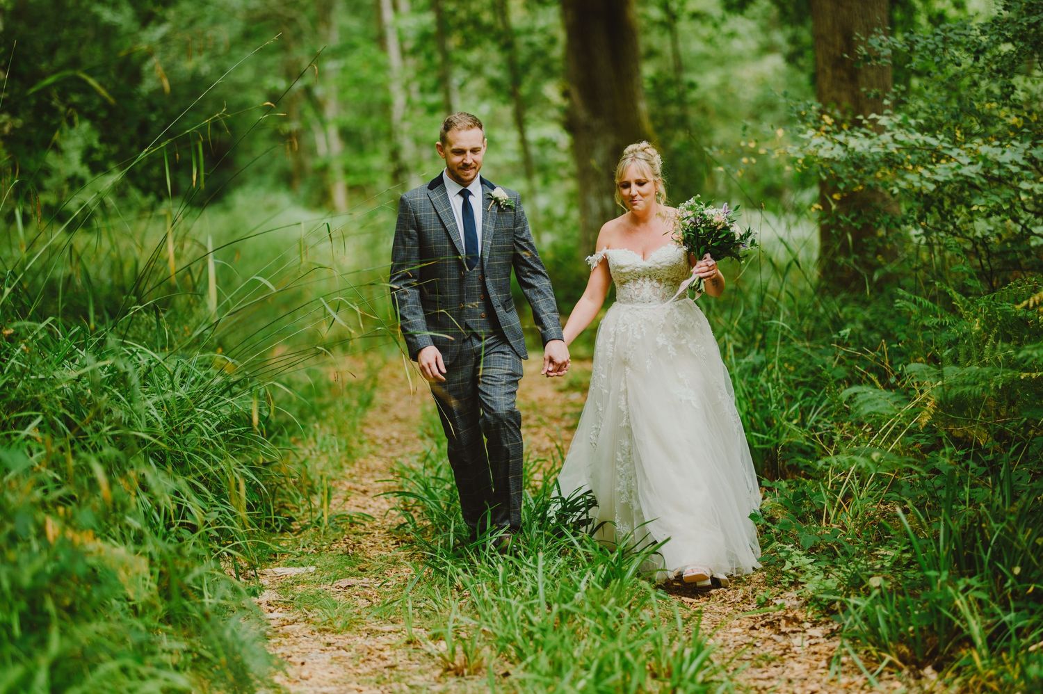 A couple strolls along a lush green garden path surrounded by vibrant summer foliage.