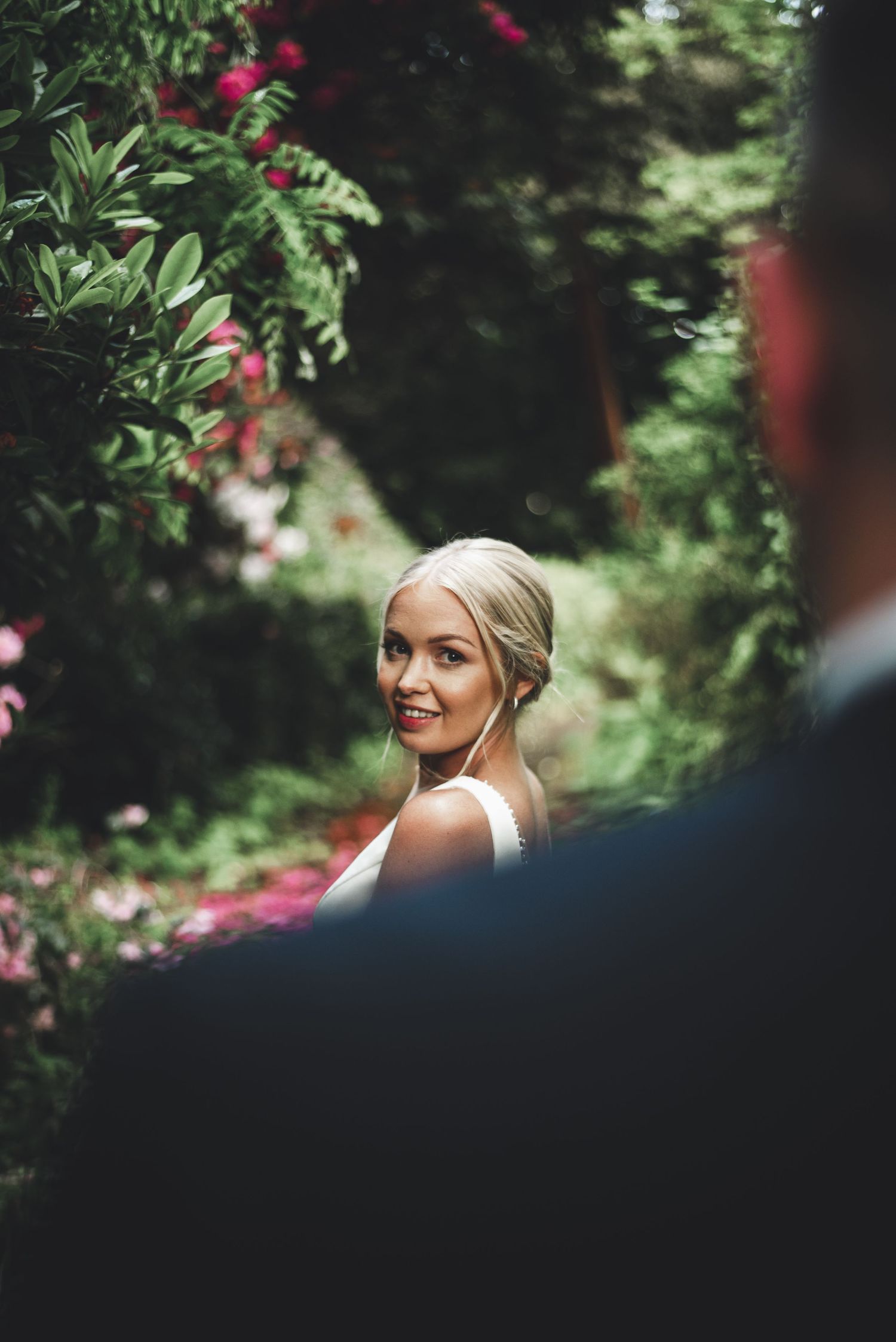 Elegant outdoor wedding portrait framed by bright red flowers and greenery.