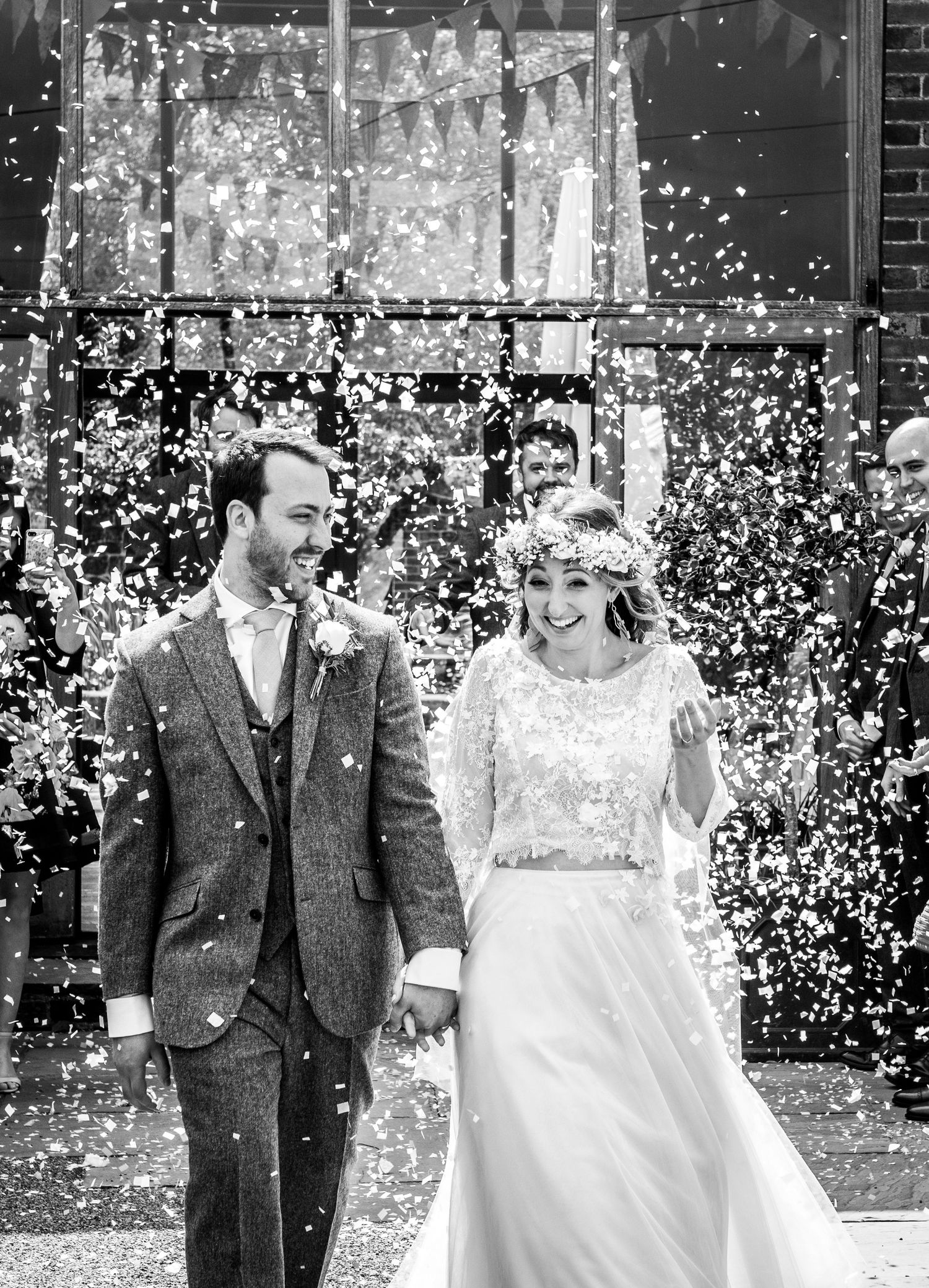 Black and white photo of newlyweds walking through shower of confetti outside church.