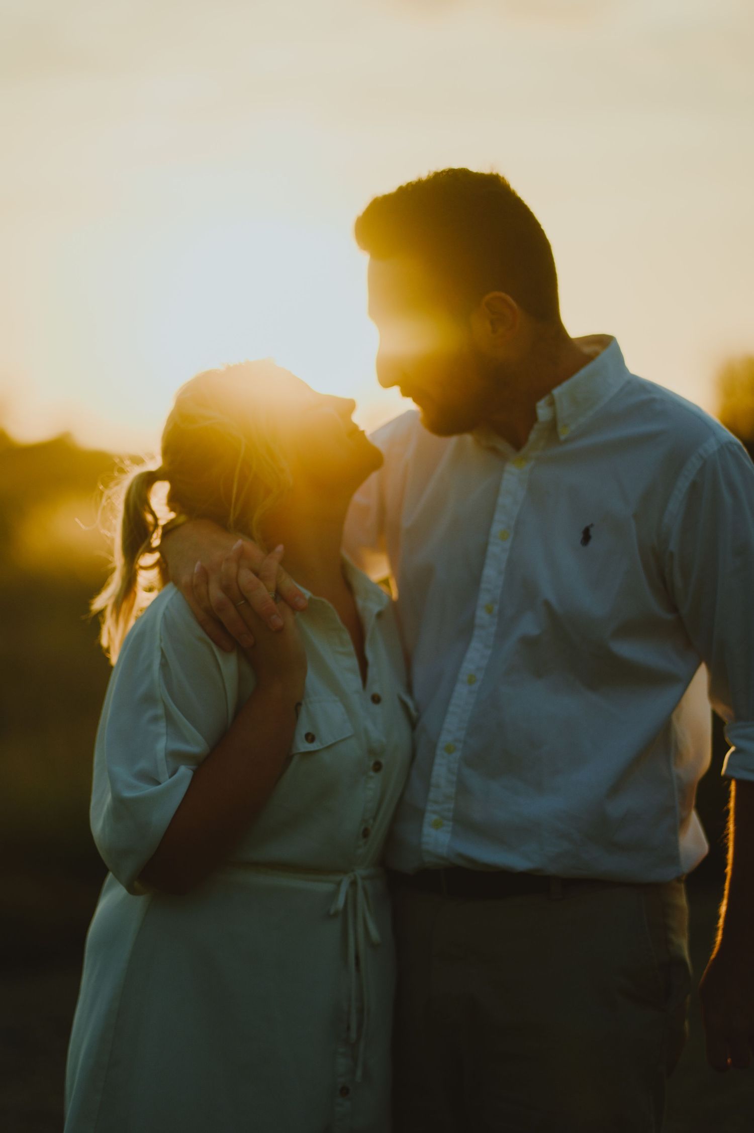 Silhouetted couple sharing an intimate moment at sunset with a golden backlight creating a romantic atmosphere.