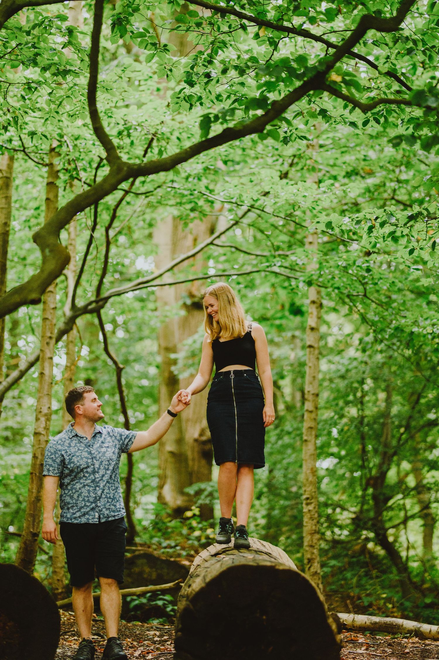 Couple enjoying a romantic moment together while sitting on a fallen tree in a lush green forest setting.