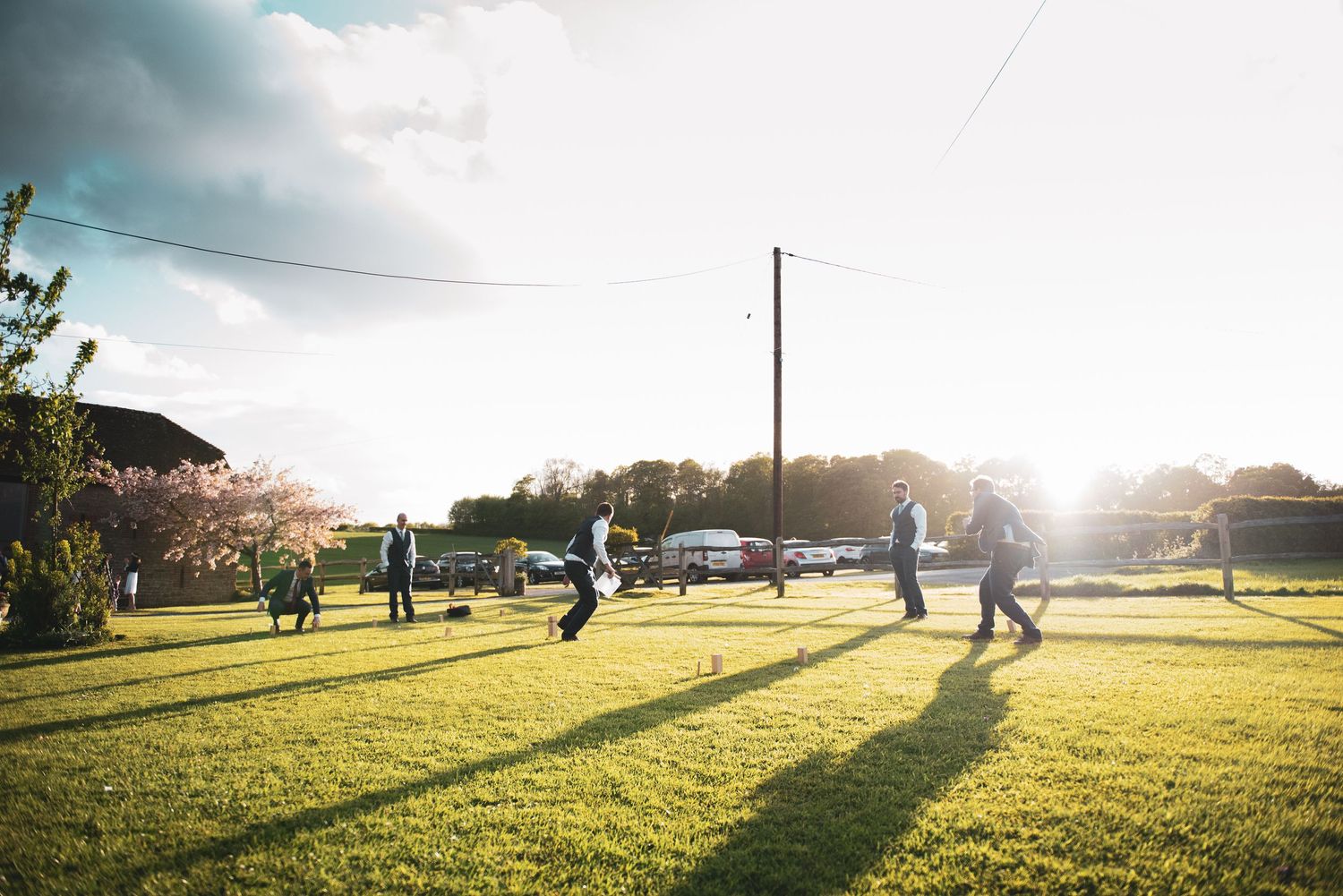 Wedding guests playing outdoor games in late afternoon sunlight on grassy lawn.