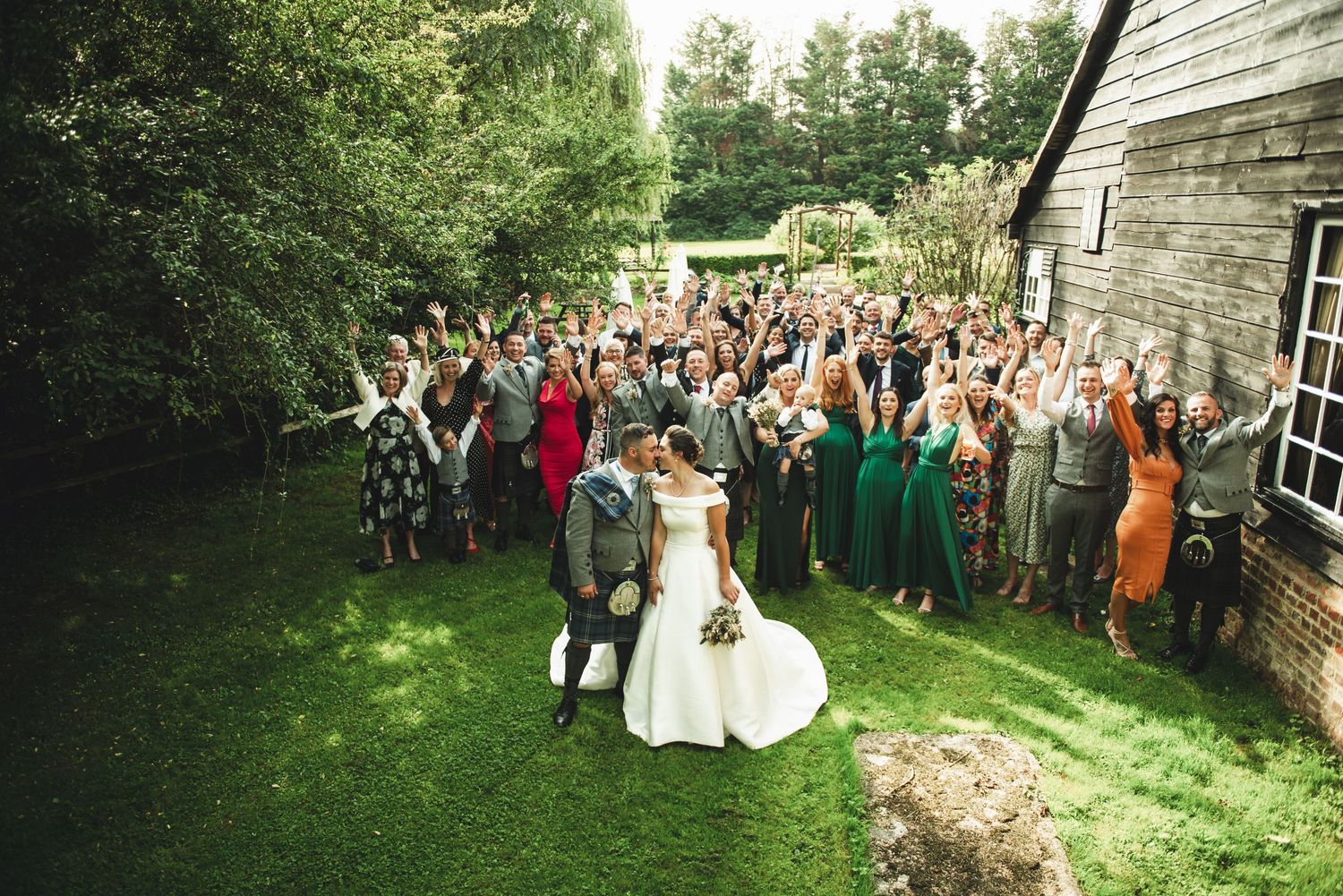 The Plough in Leigh Kent wedding venue A large wedding party celebrates outdoors in front of a rustic barn with guests