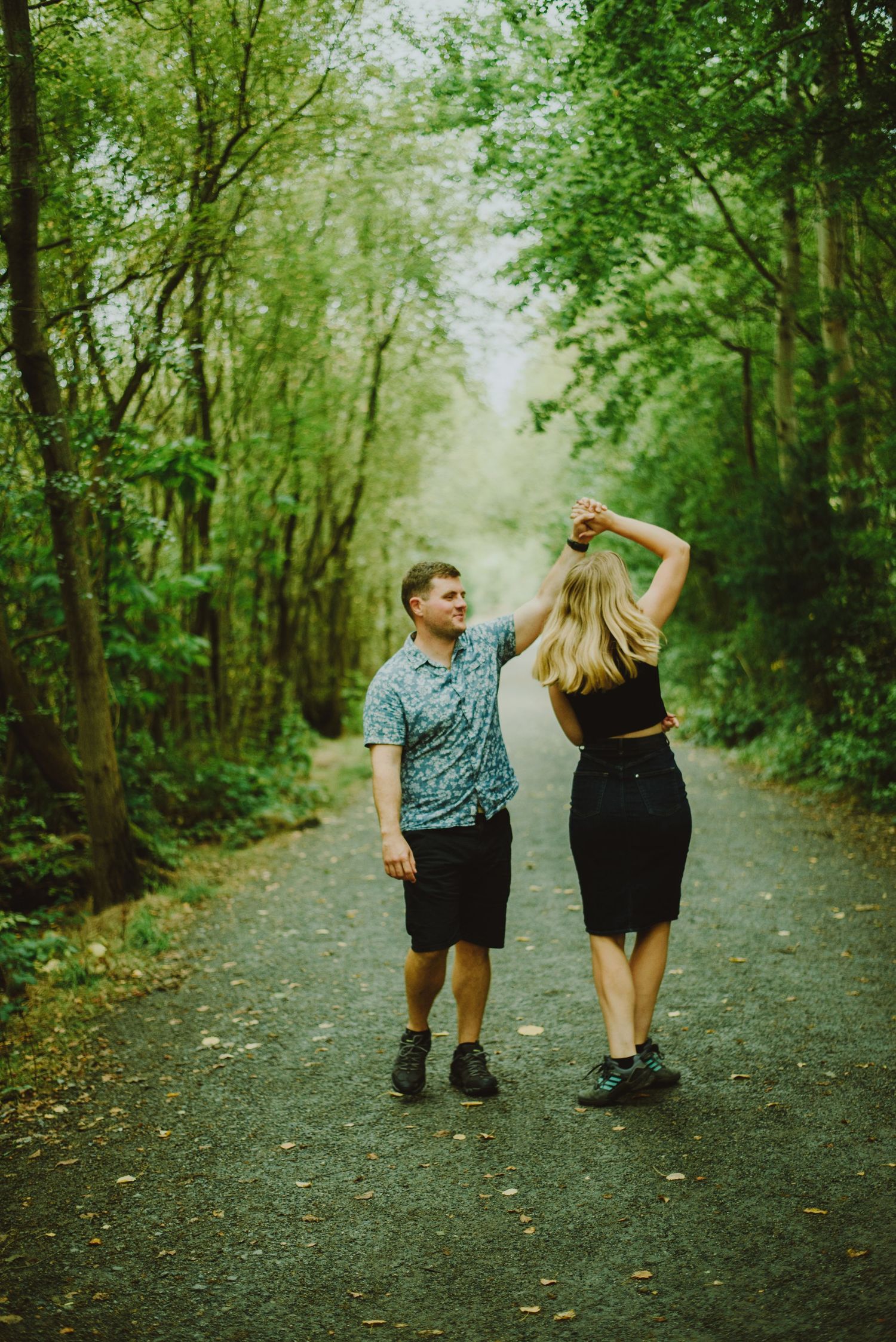 A couple walking hand in hand down a serene tree-lined path during an outdoor photo session.