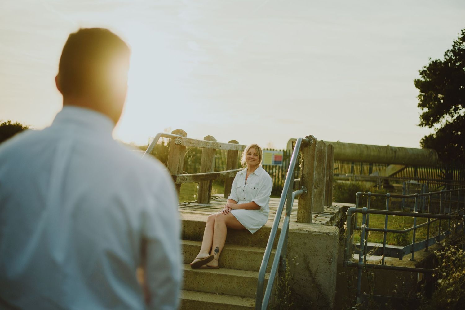 A couple shares a tender moment in a field during golden hour with a rural backdrop.
