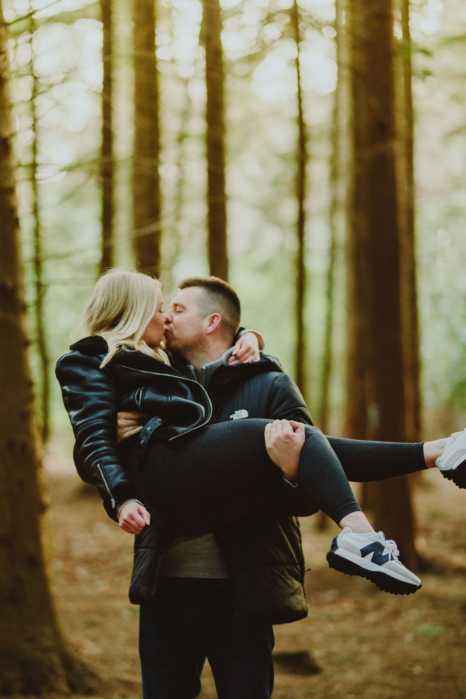 A romantic couple shares a tender kiss in a misty forest as one carries the other in their arms.