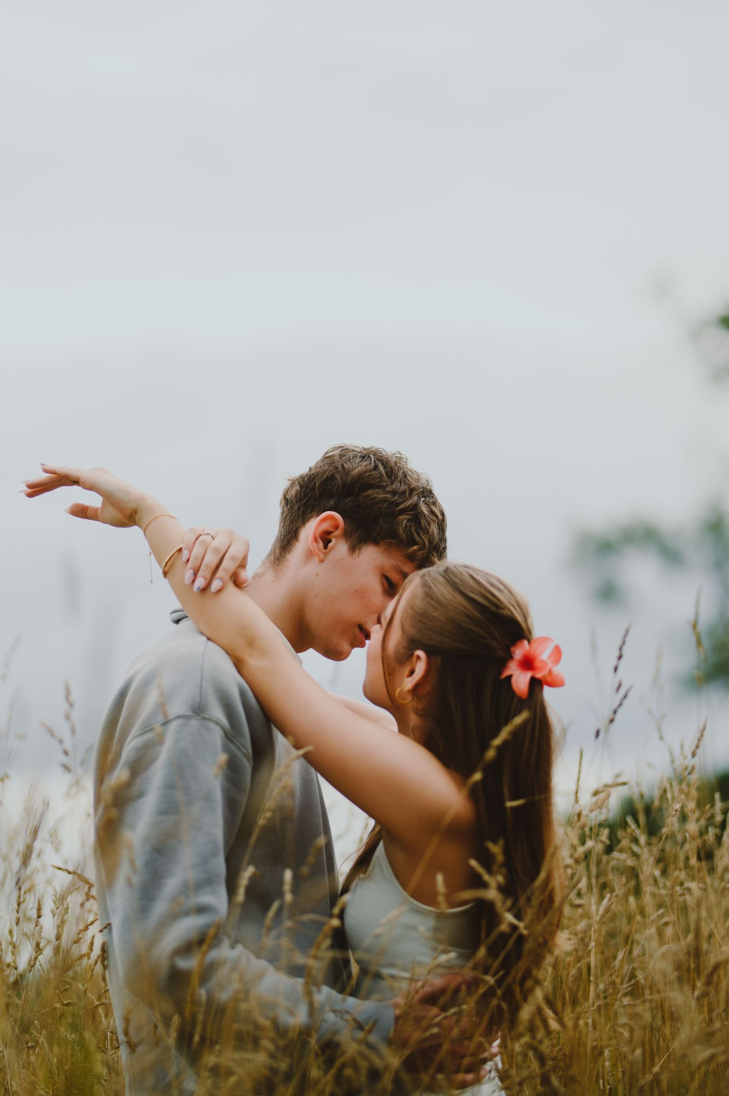 A couple shares an intimate embrace while standing in a golden field of tall grass during sunset.