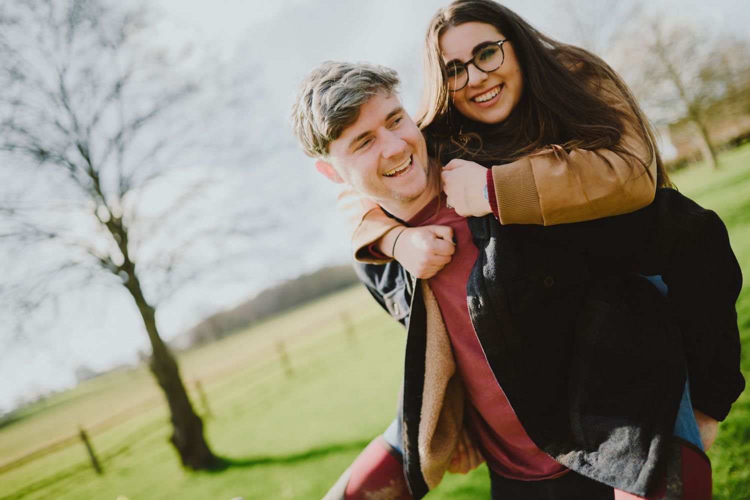 A couple laughs together while embracing outdoors during a winter photoshoot in a park.