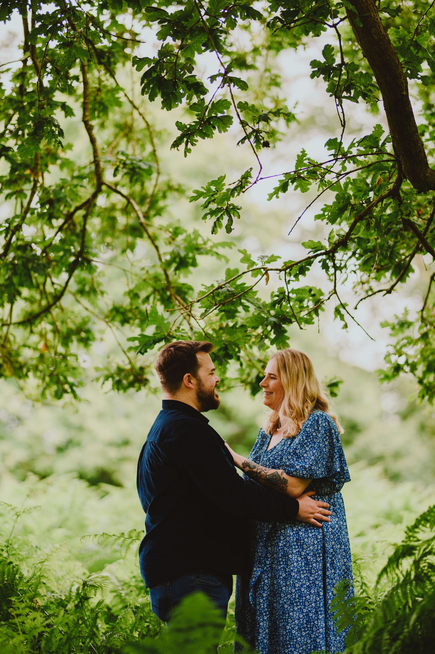 A loving couple embraces under green tree branches in a romantic outdoor setting during spring.