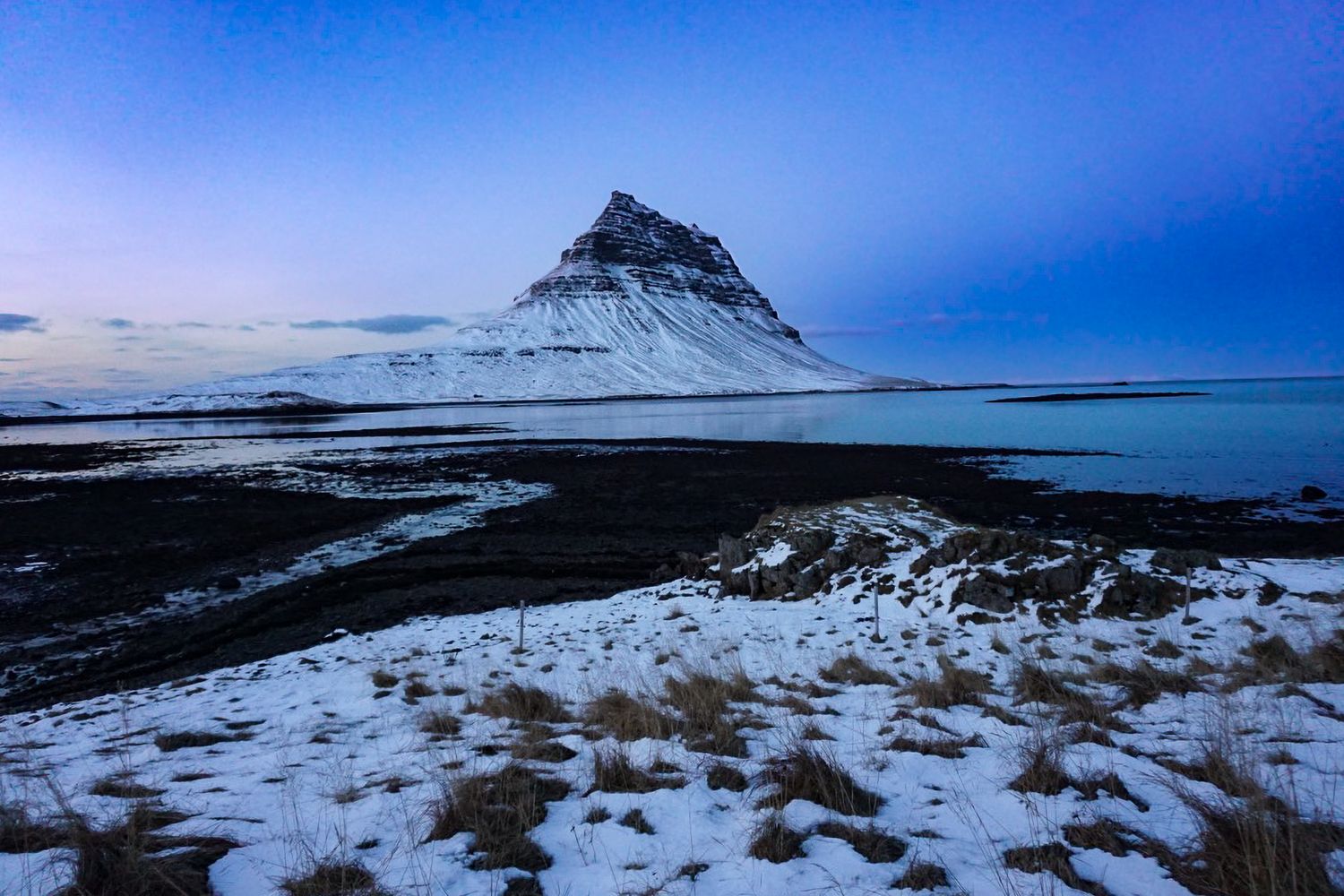 Snow-covered Kirkjufell mountain in Iceland under a stunning blue twilight winter sky.