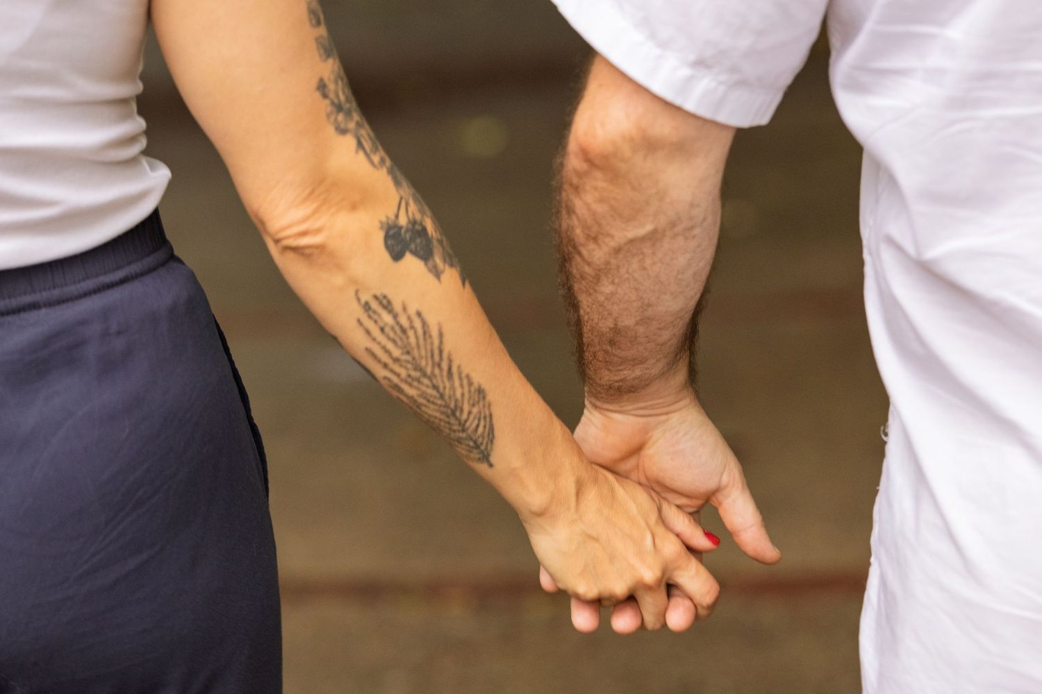 Close-up of two people holding hands, one with a feather tattoo on their forearm.