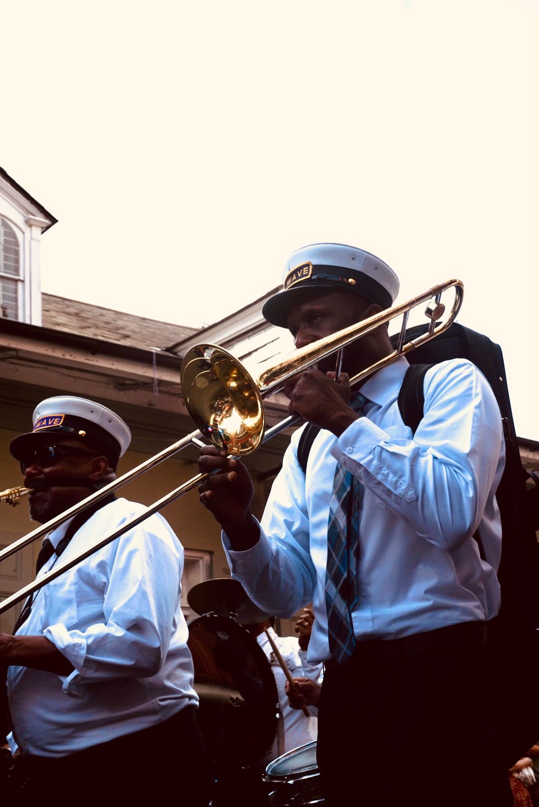Two brass band musicians in white shirts, ties and white captain caps play trombone and drums during a street parade.