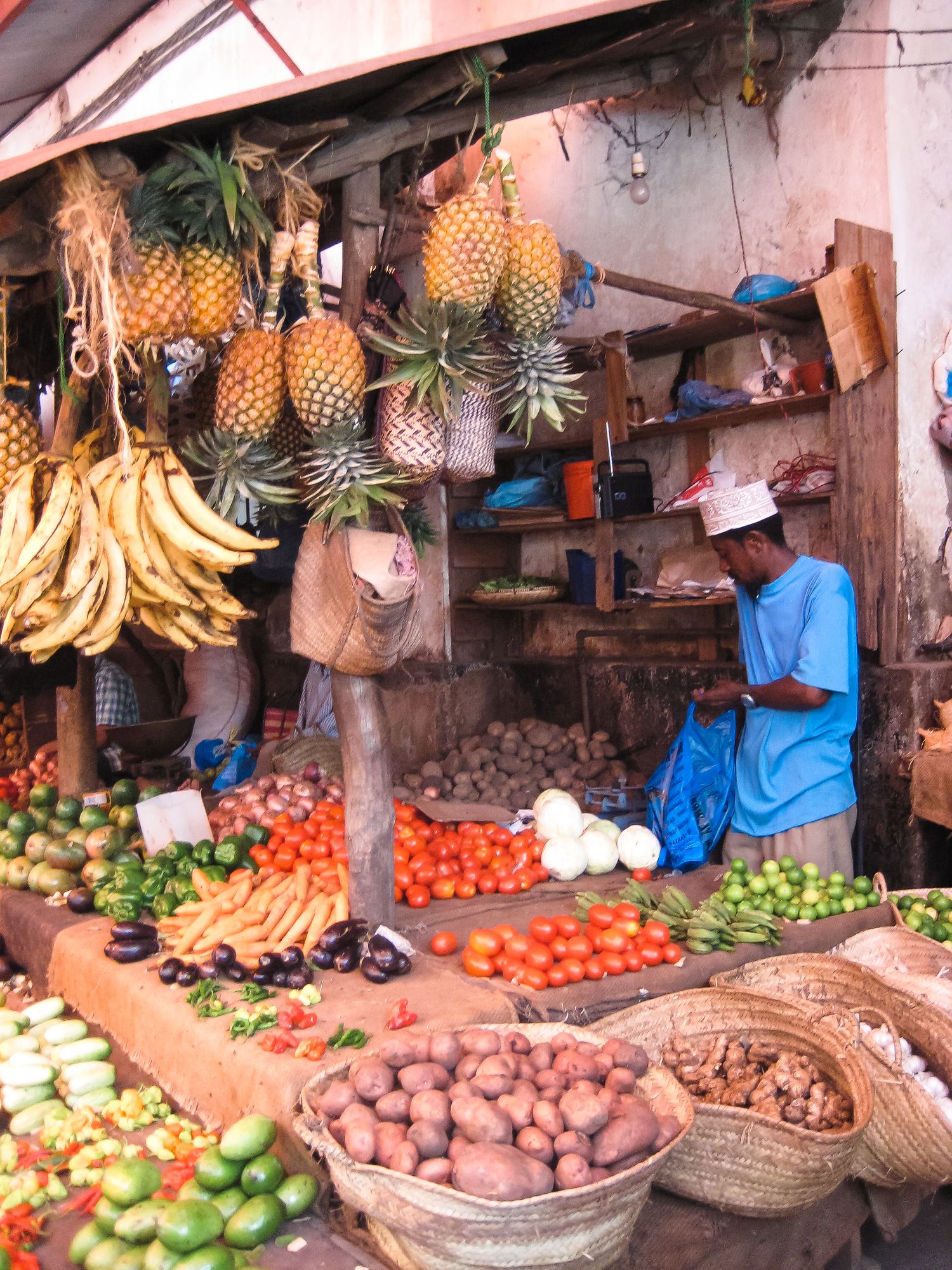 A vibrant African market stall displays fresh pineapples, bananas, tomatoes, and vegetables with a vendor.