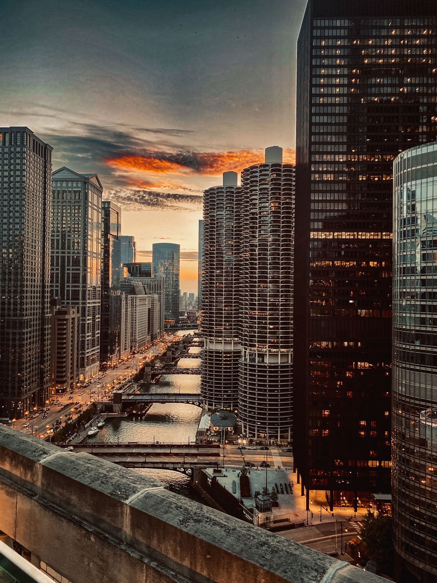 A dramatic Chicago River sunset skyline view with glowing skyscrapers reflecting warm orange clouds above.