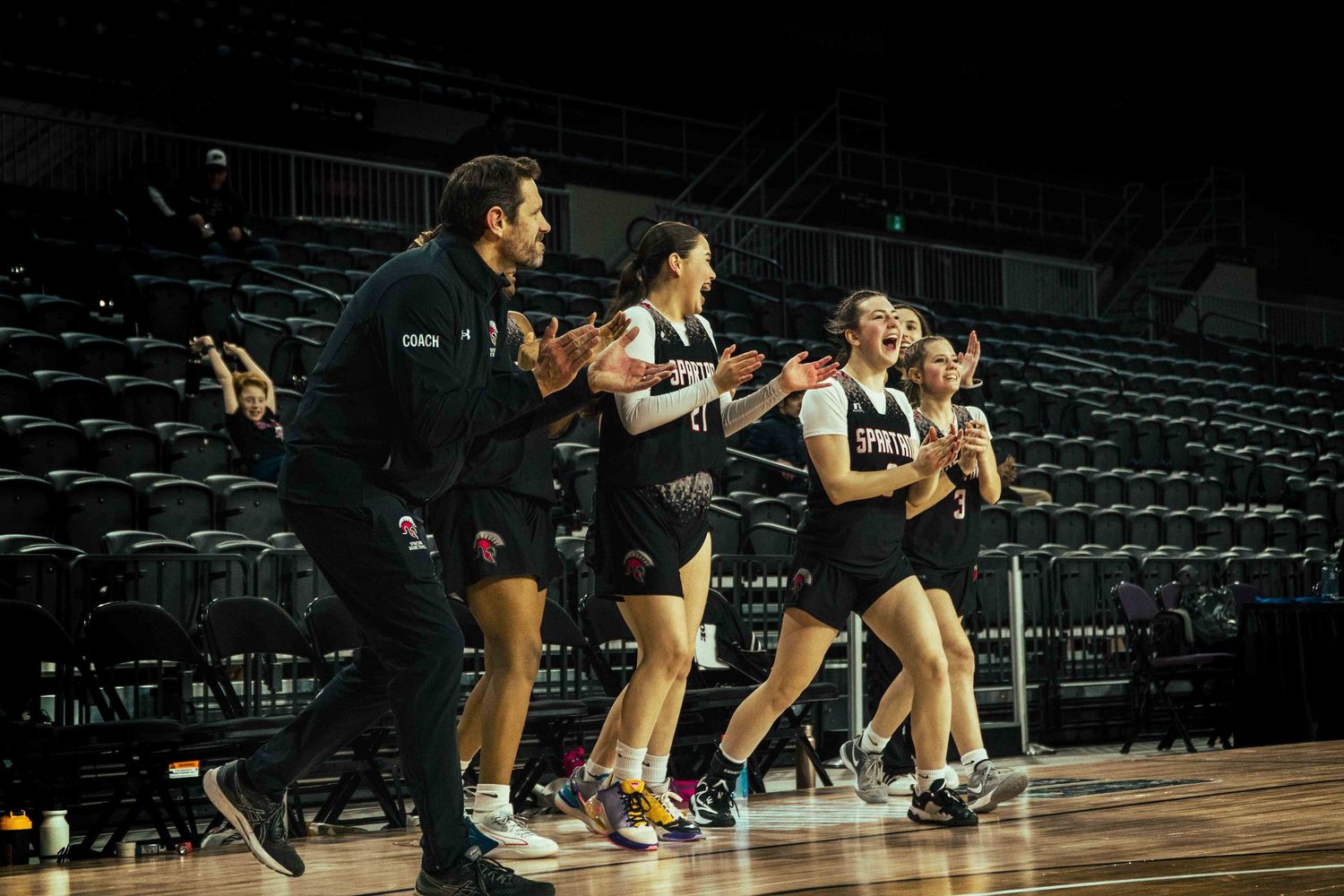 Basketball players and coaches react enthusiastically from the sidelines during a game.