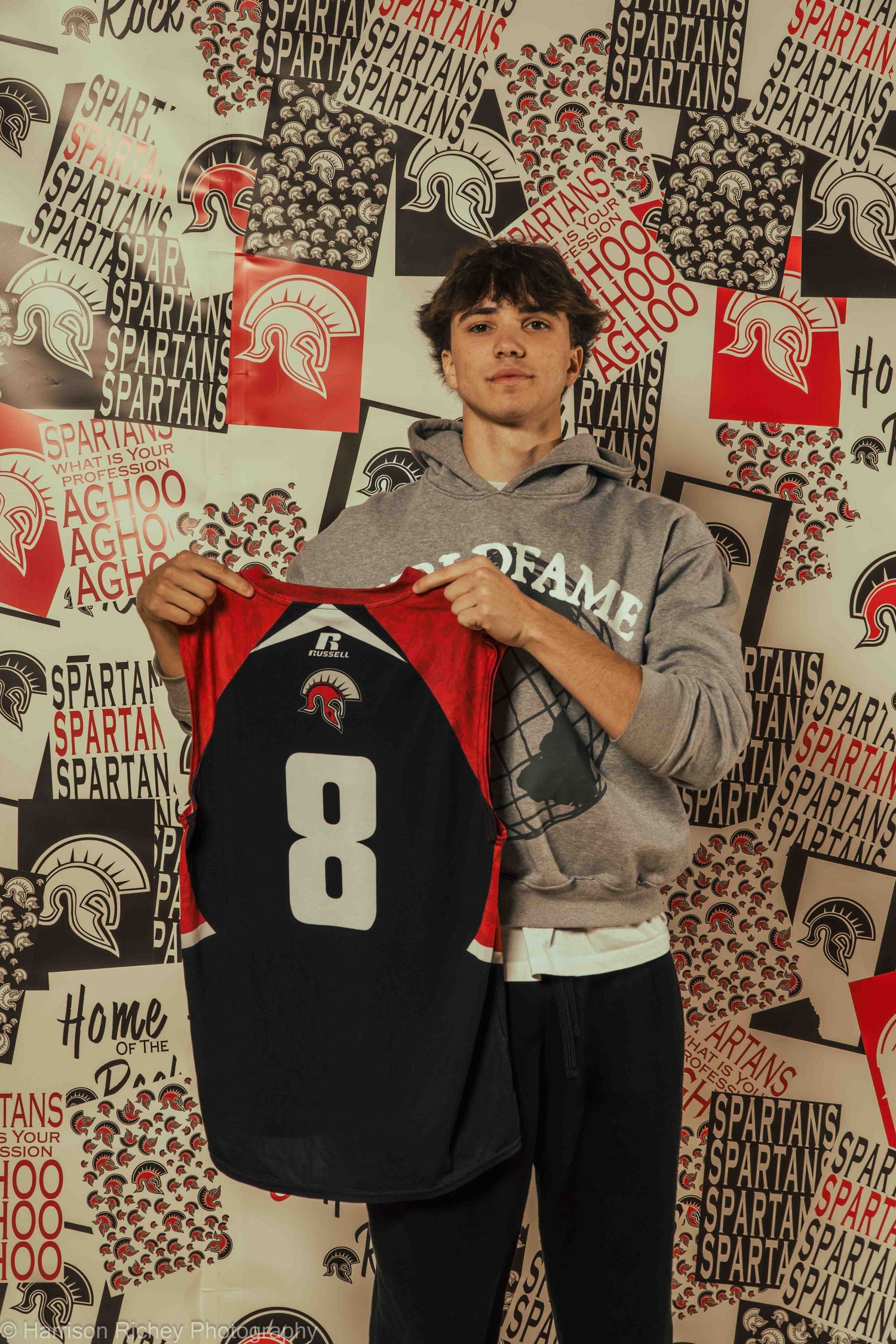 Team members display black basketball jerseys against decorative Spartan-themed wall background.