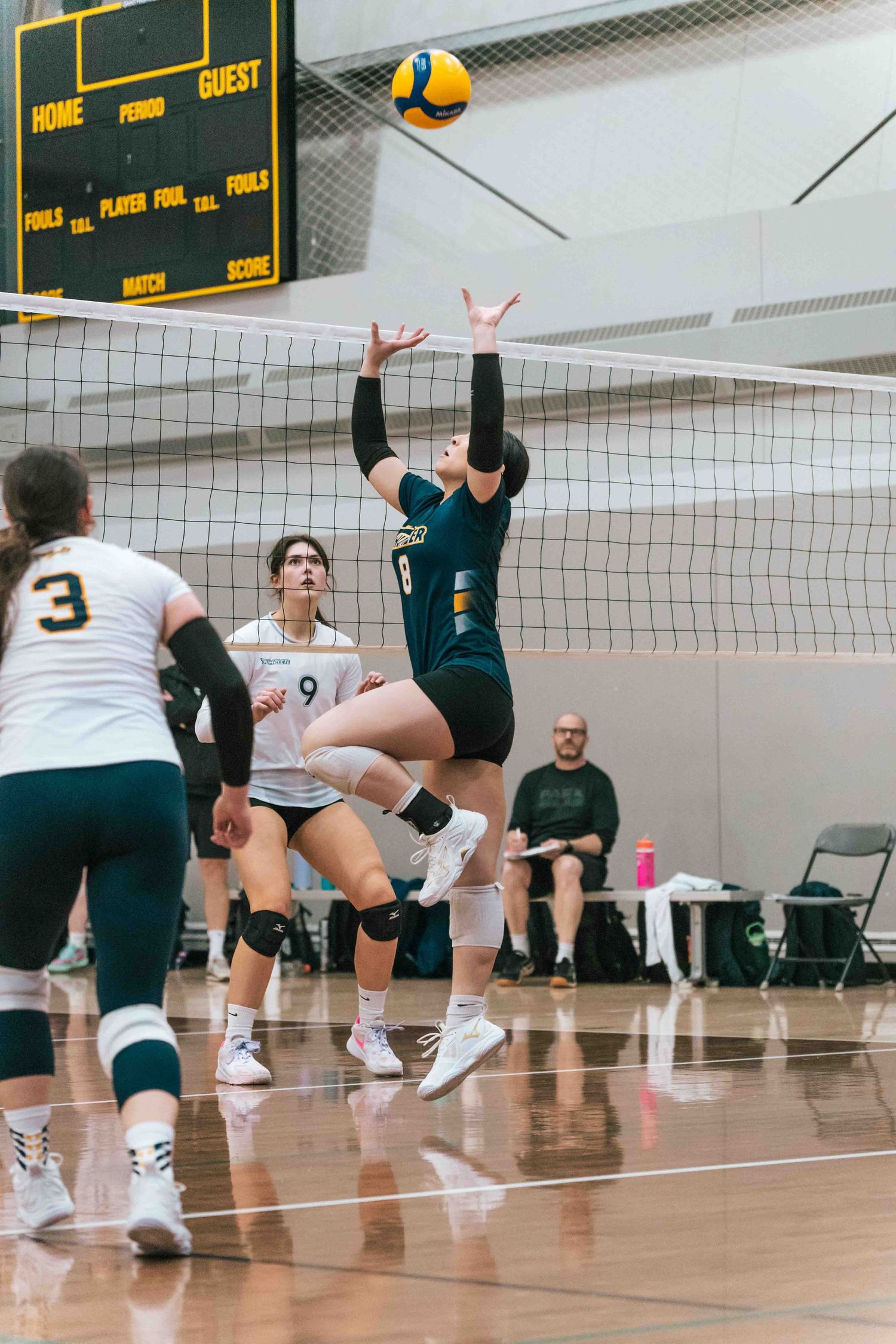 Volleyball players from opposing teams jump at the net during an indoor match.