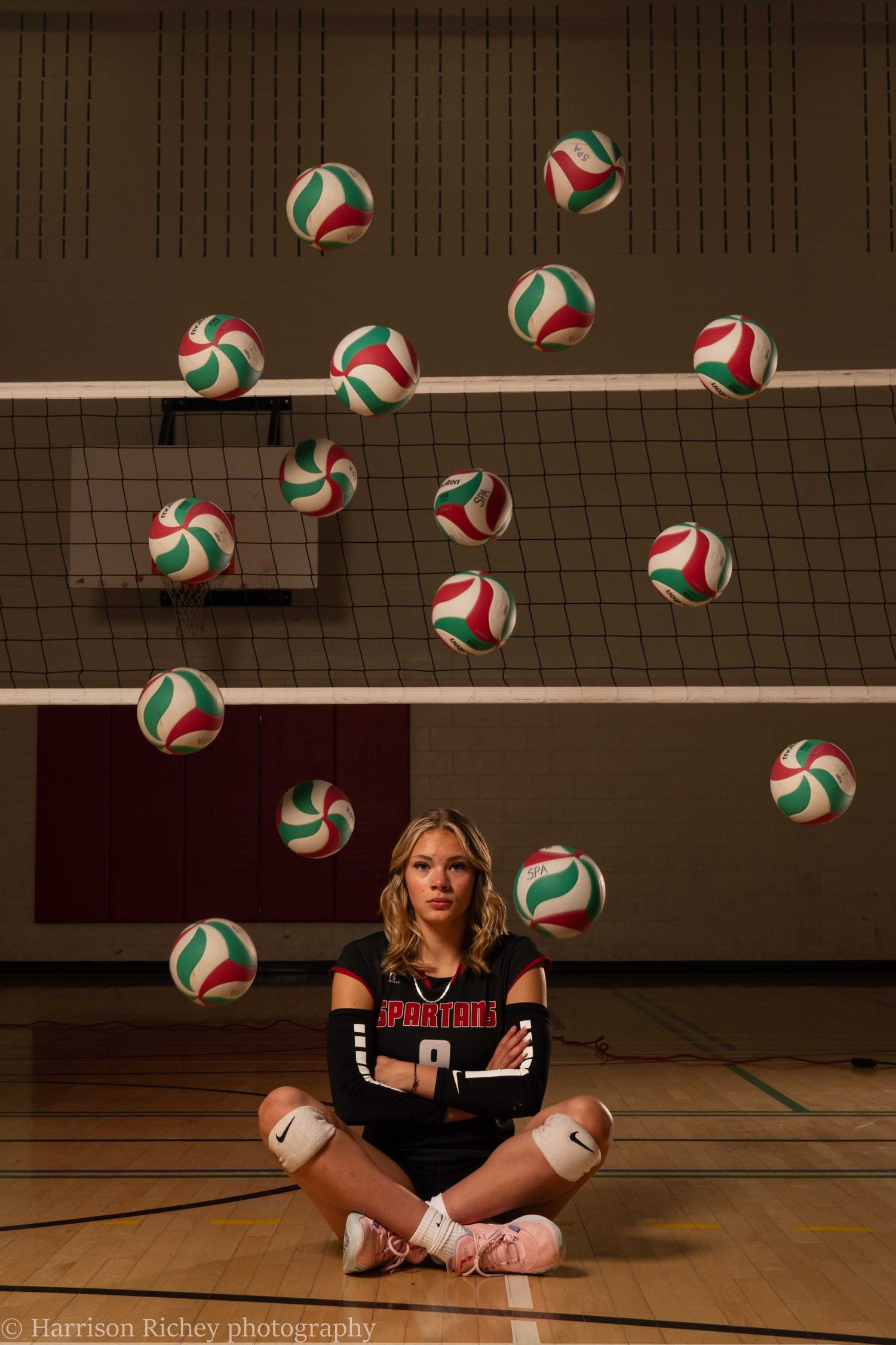 Creative sports portrait of a volleyball player sitting with multiple floating game balls in a gymnasium.