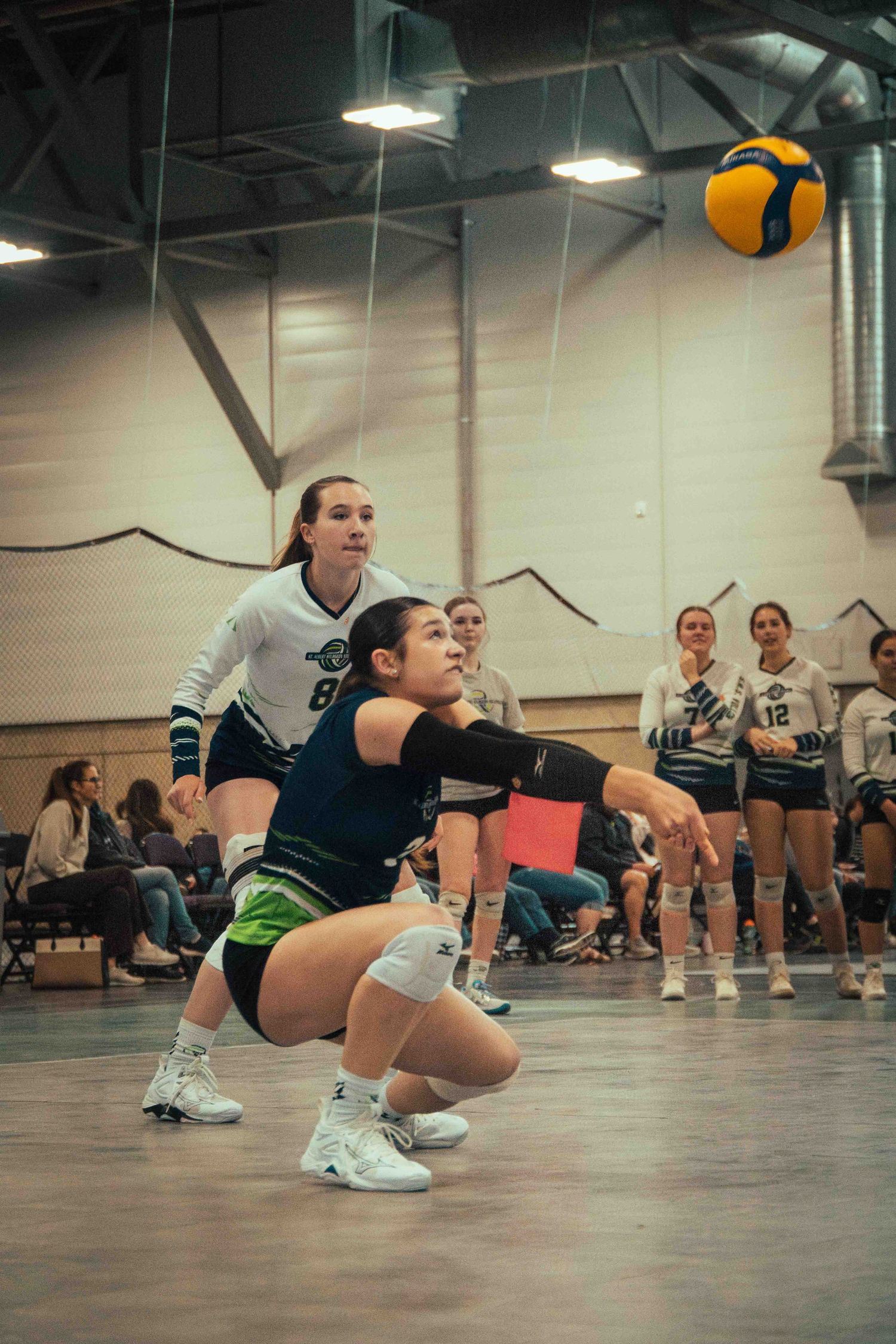 Volleyball players in defensive position tracking the ball during indoor match play.