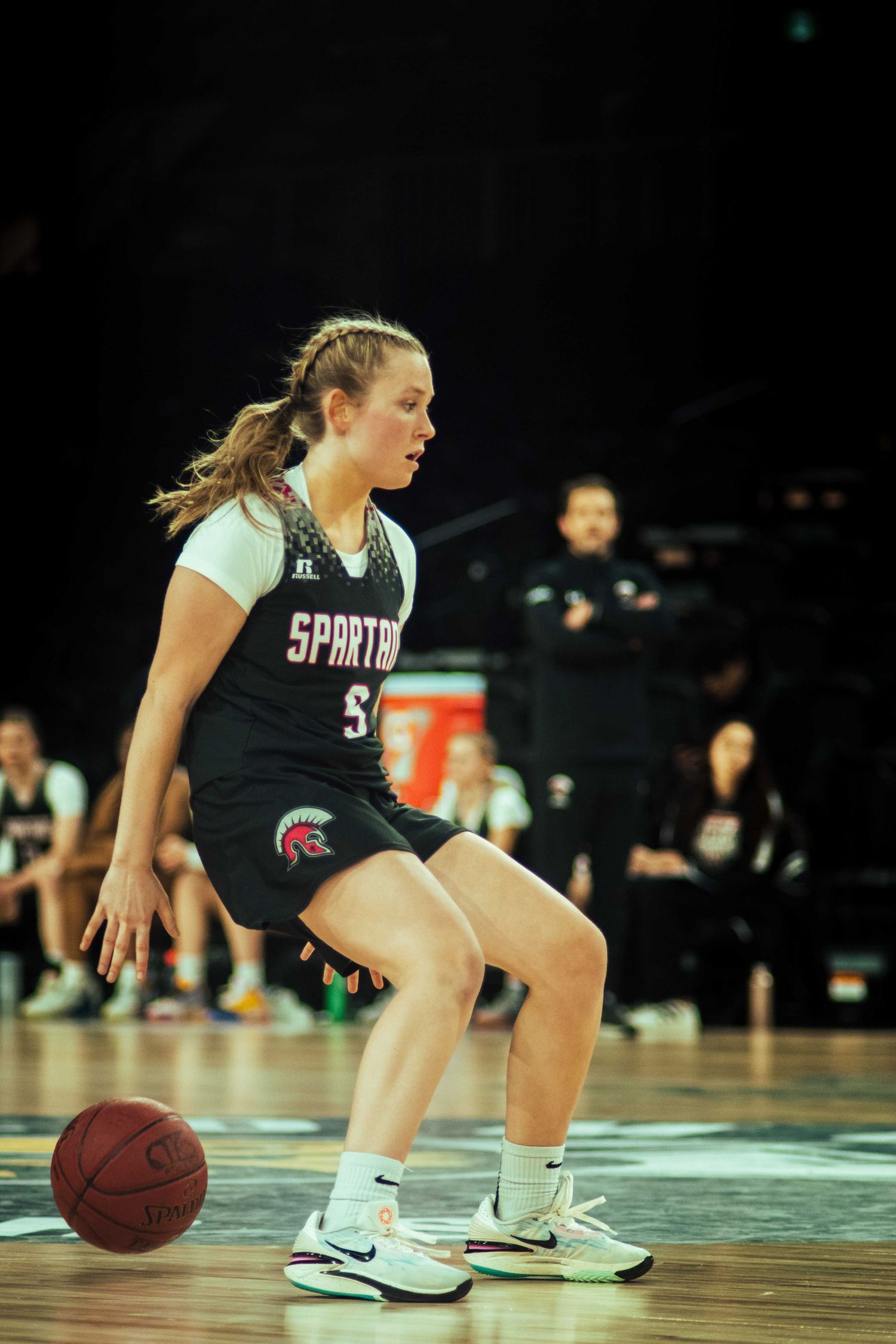 Basketball player dribbles while maintaining defensive stance during game.