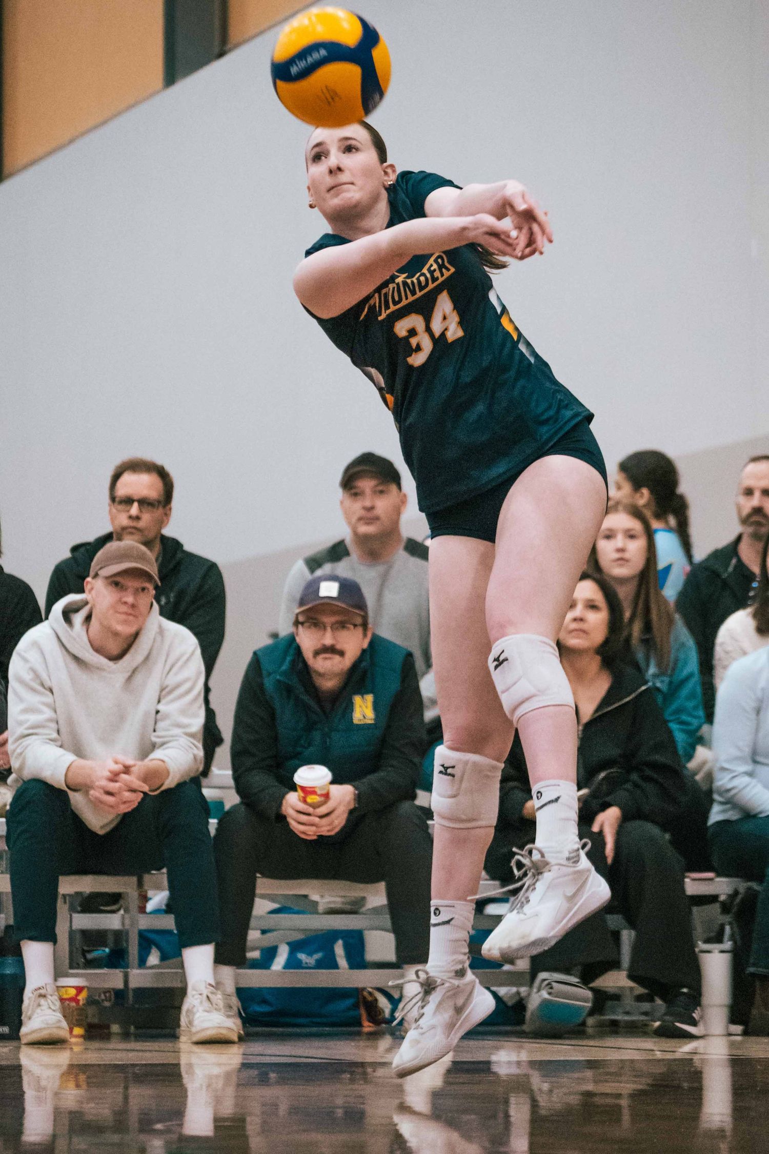 Volleyball player wearing number 34 prepares to pass during indoor match with spectators watching.