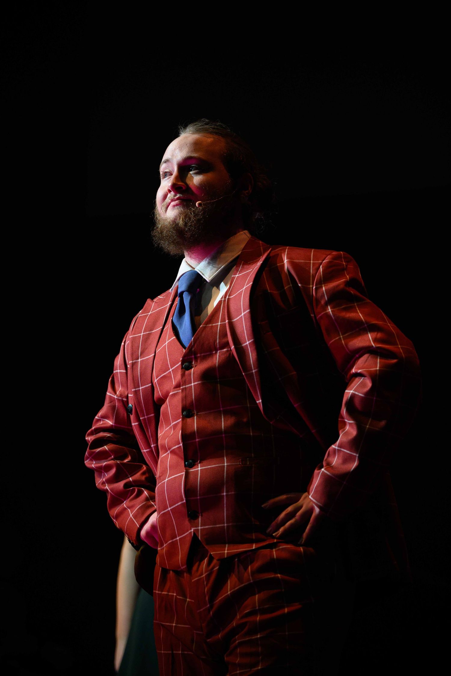 A dramatic performance on stage featuring a person in a plaid red suit against a dark background.