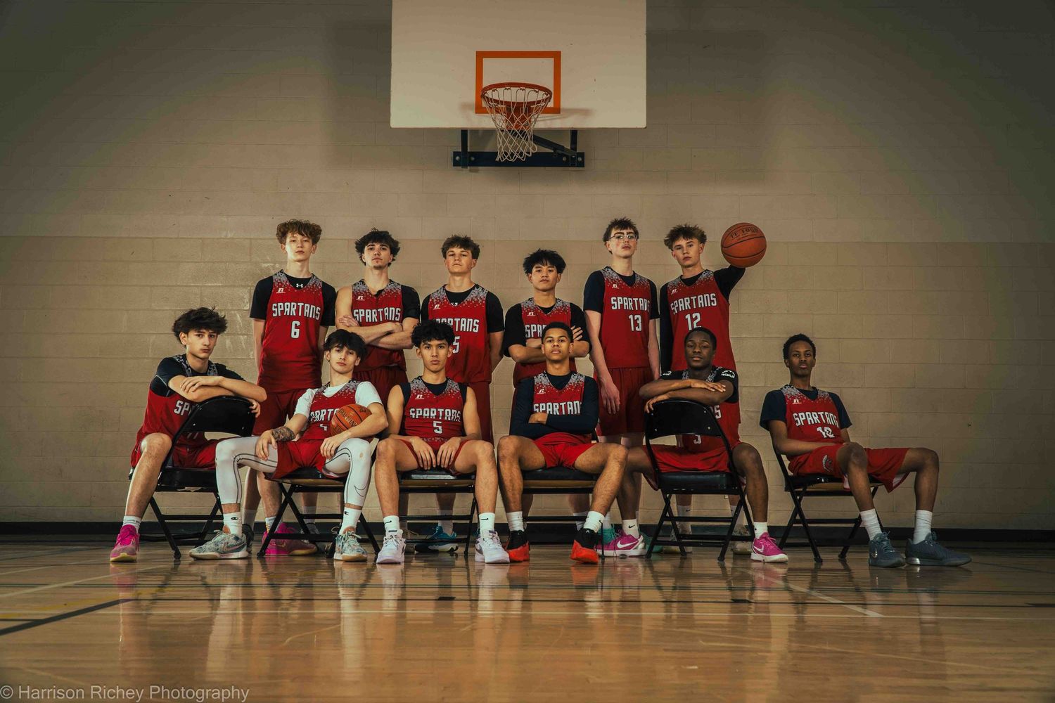 Basketball team poses for official photo on indoor court with hoop in background.