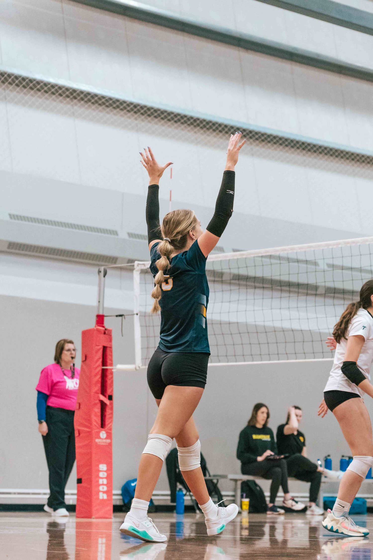 Player in dark jersey raises their arms in celebration in a indoor volleyball match