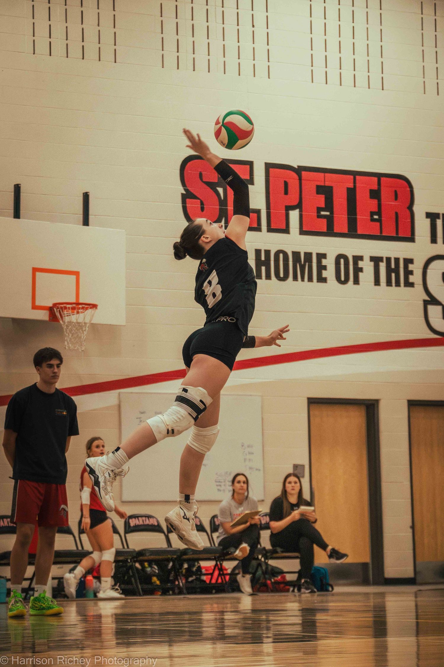A volleyball player leaps high to spike the ball during a game at St. Peter's gymnasium.