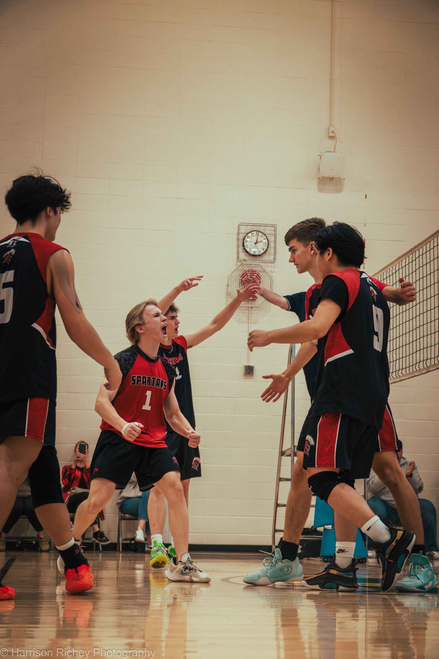 Athletes compete in a volleyball match with players diving and stretching for the ball on a gymnasium court.