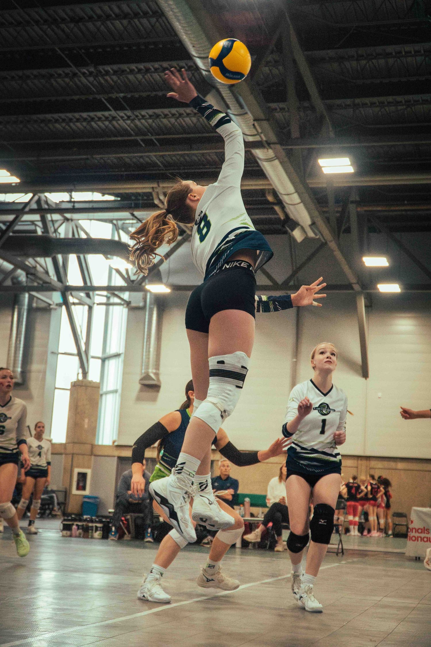 Athletic volleyball player jumping to hit the ball during competitive indoor match.