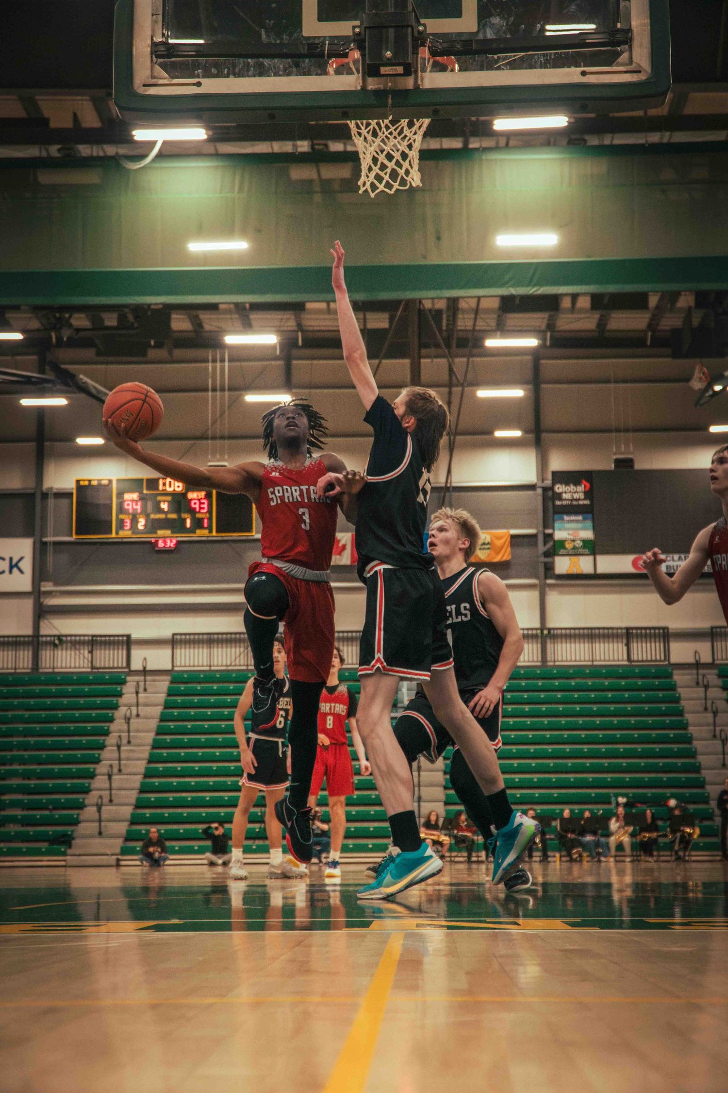 Basketball players leap high for a contested shot under the basket.
