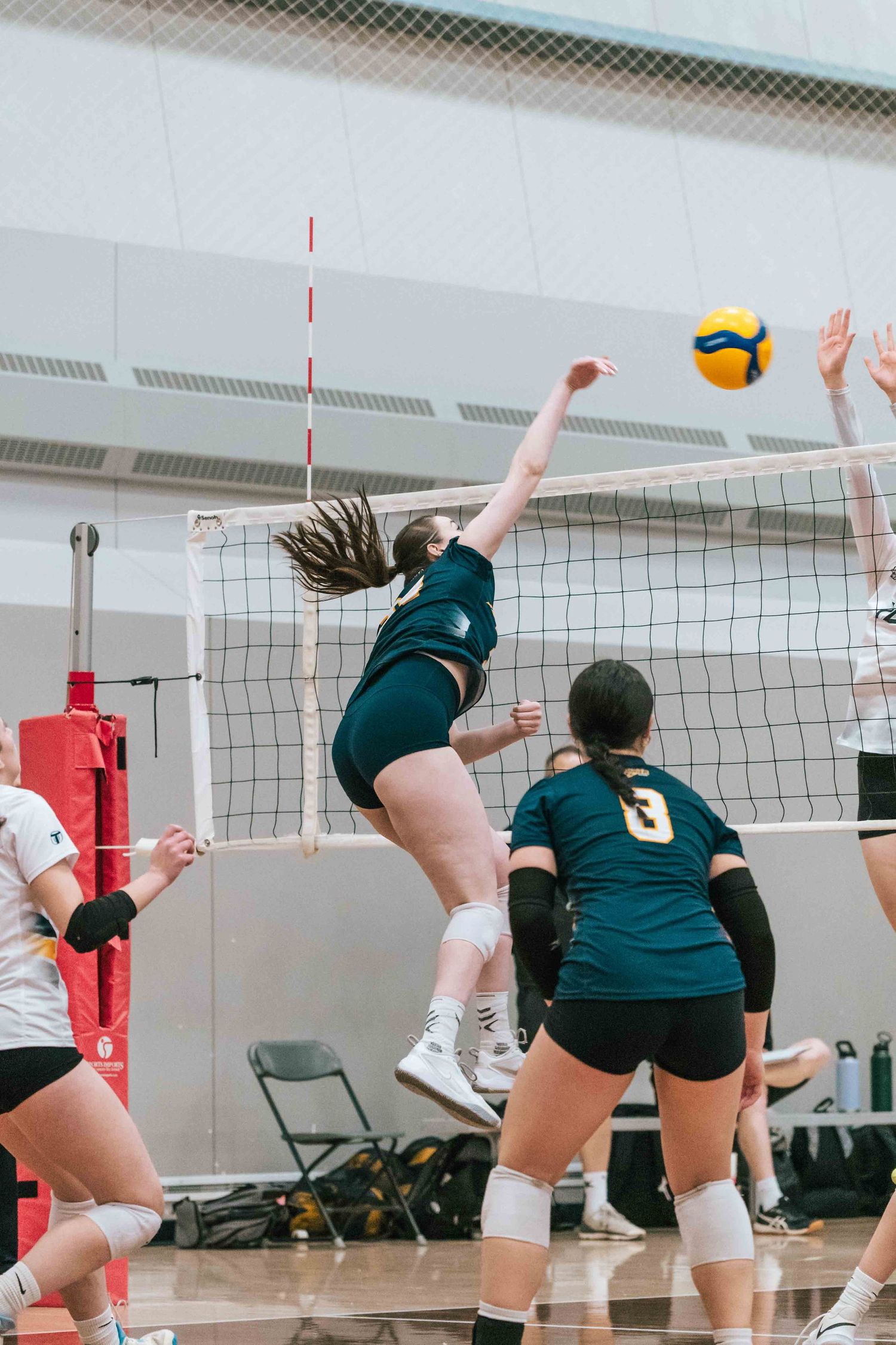 Player leaps high to spike volleyball during intense indoor match at gymnasium.