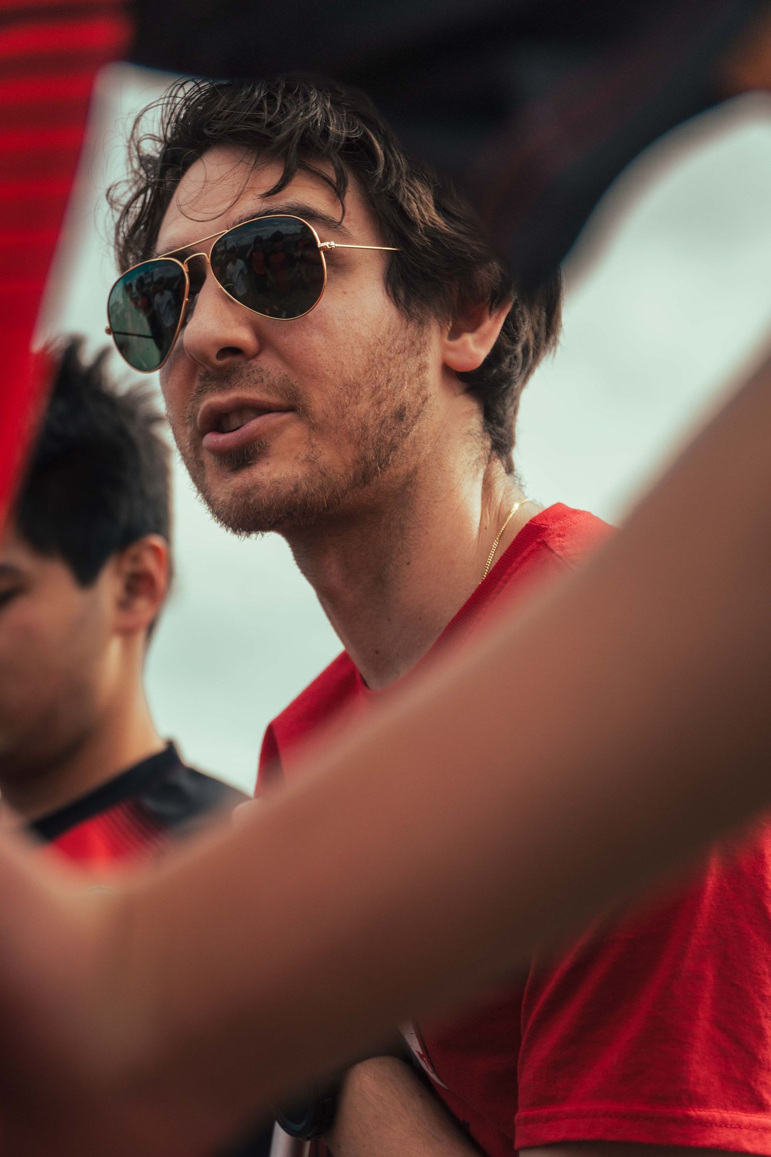 Person in aviator sunglasses and red shirt photographed in profile against a blurred background.