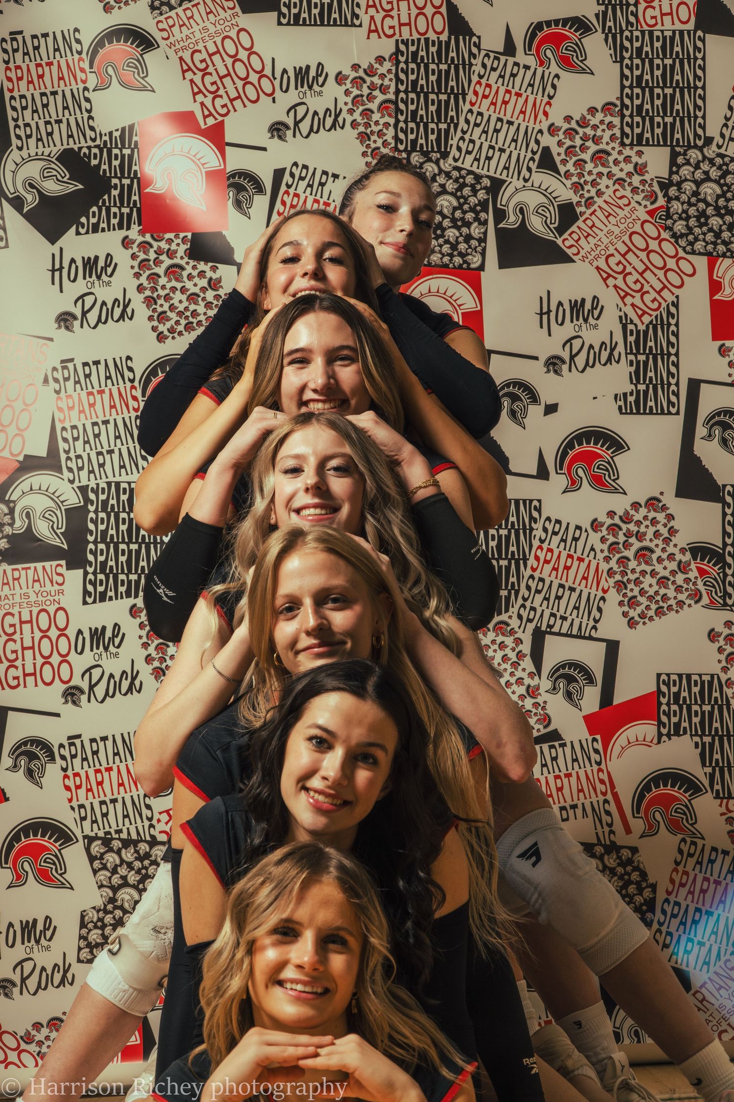 Group photo of cheerleaders posing together against a wall decorated with team spirit graphics and logos.