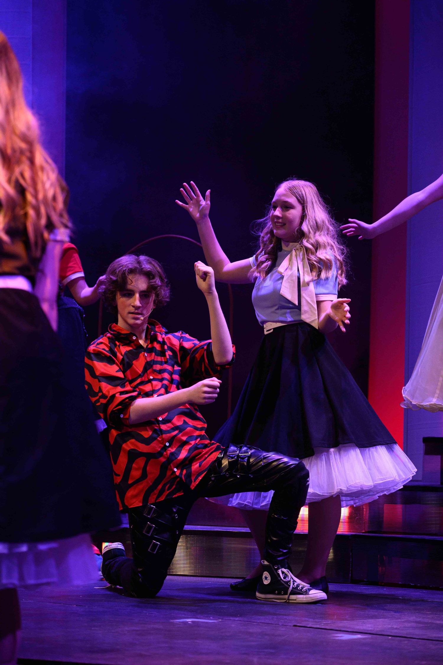 Dancers perform low to the ground under purple stage lighting.