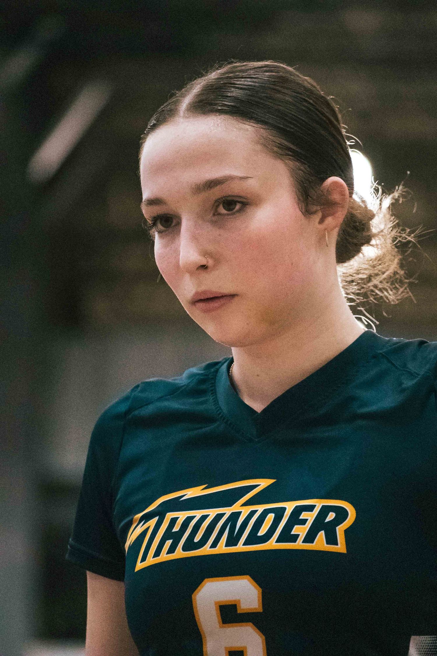 Volleyball player in dark green jersey poses for portrait against blurred background.