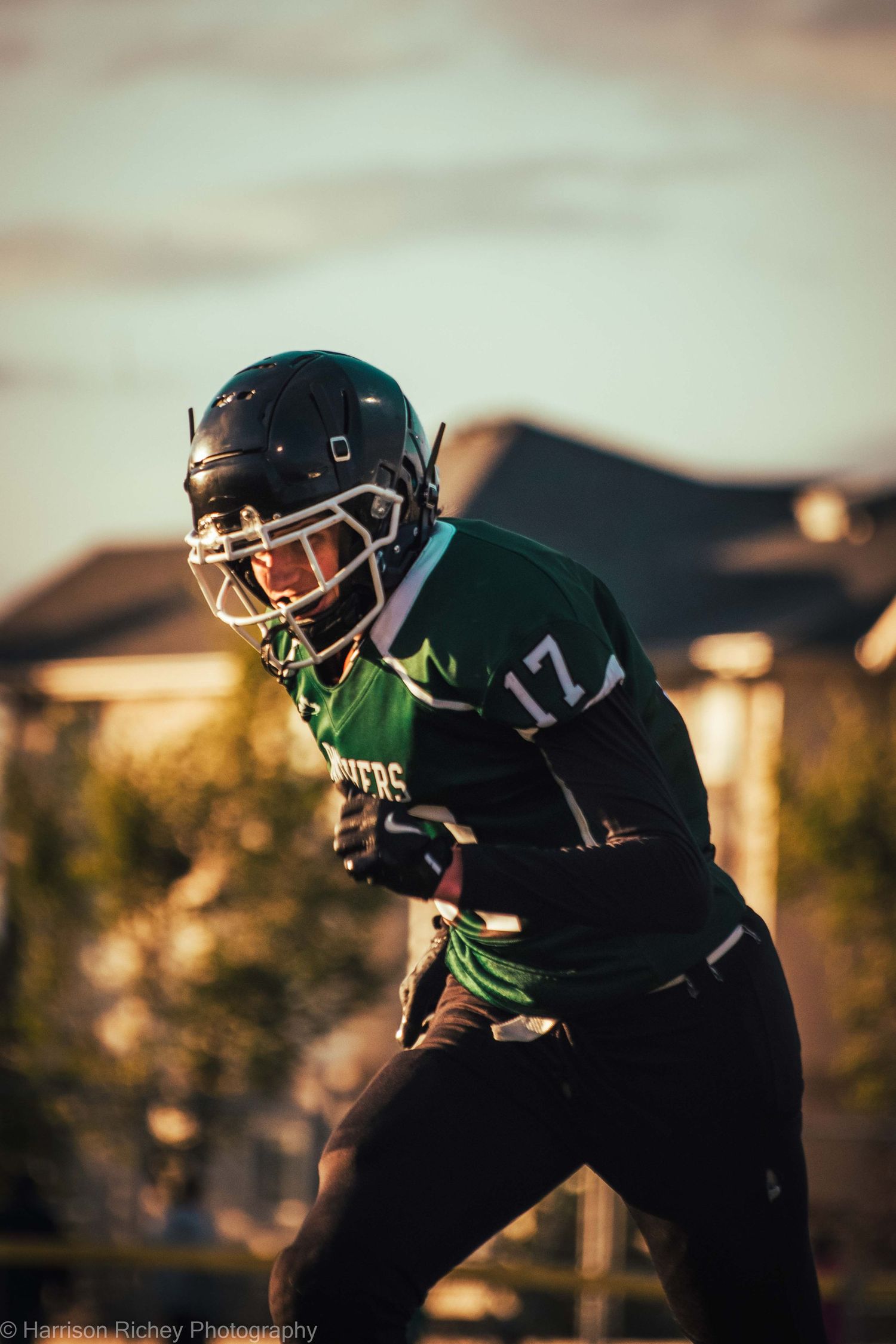 Football player in dark uniform stands ready in golden sunset light.