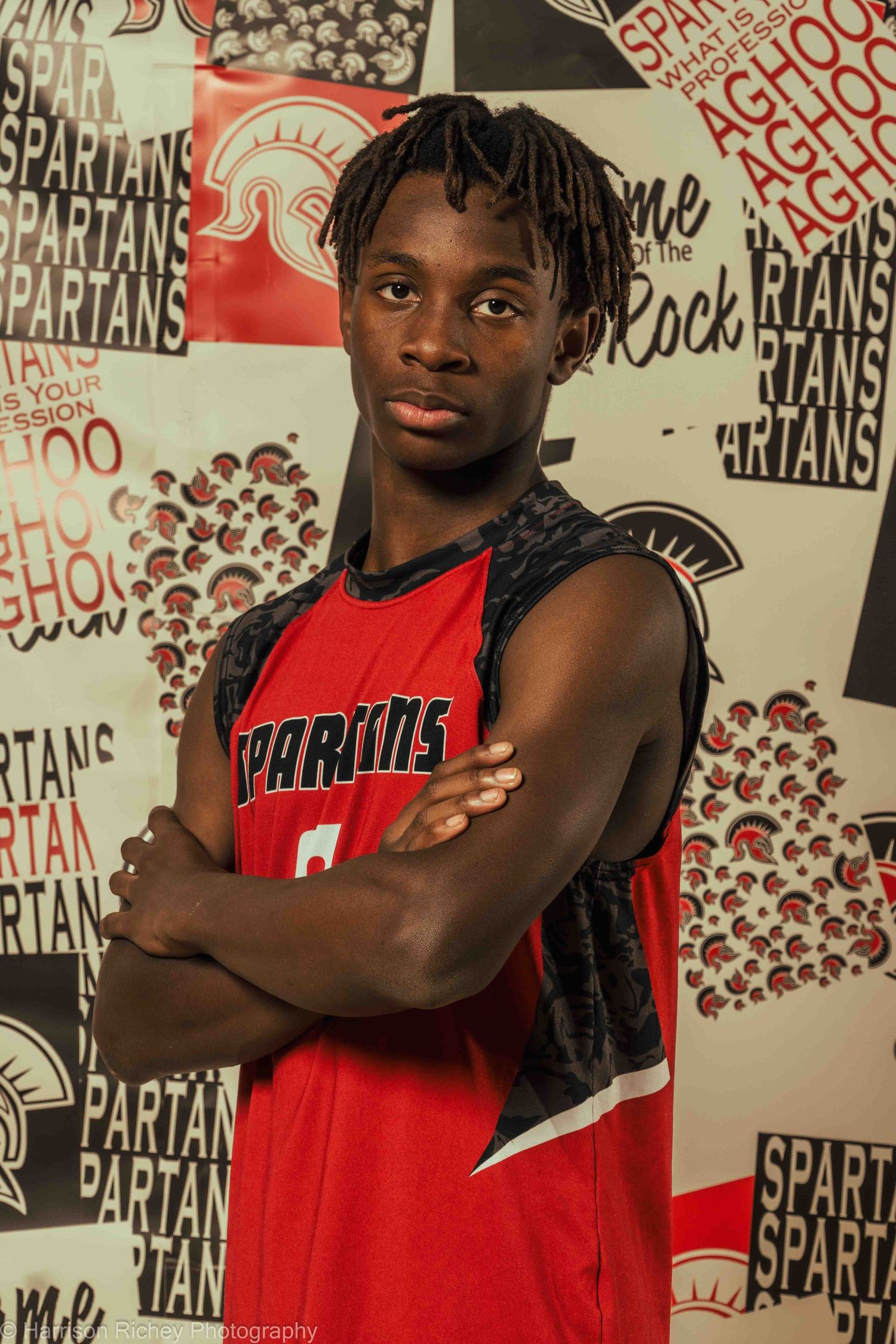 Athletes in red team uniforms pose confidently against decorated wall with Spartan graphics.