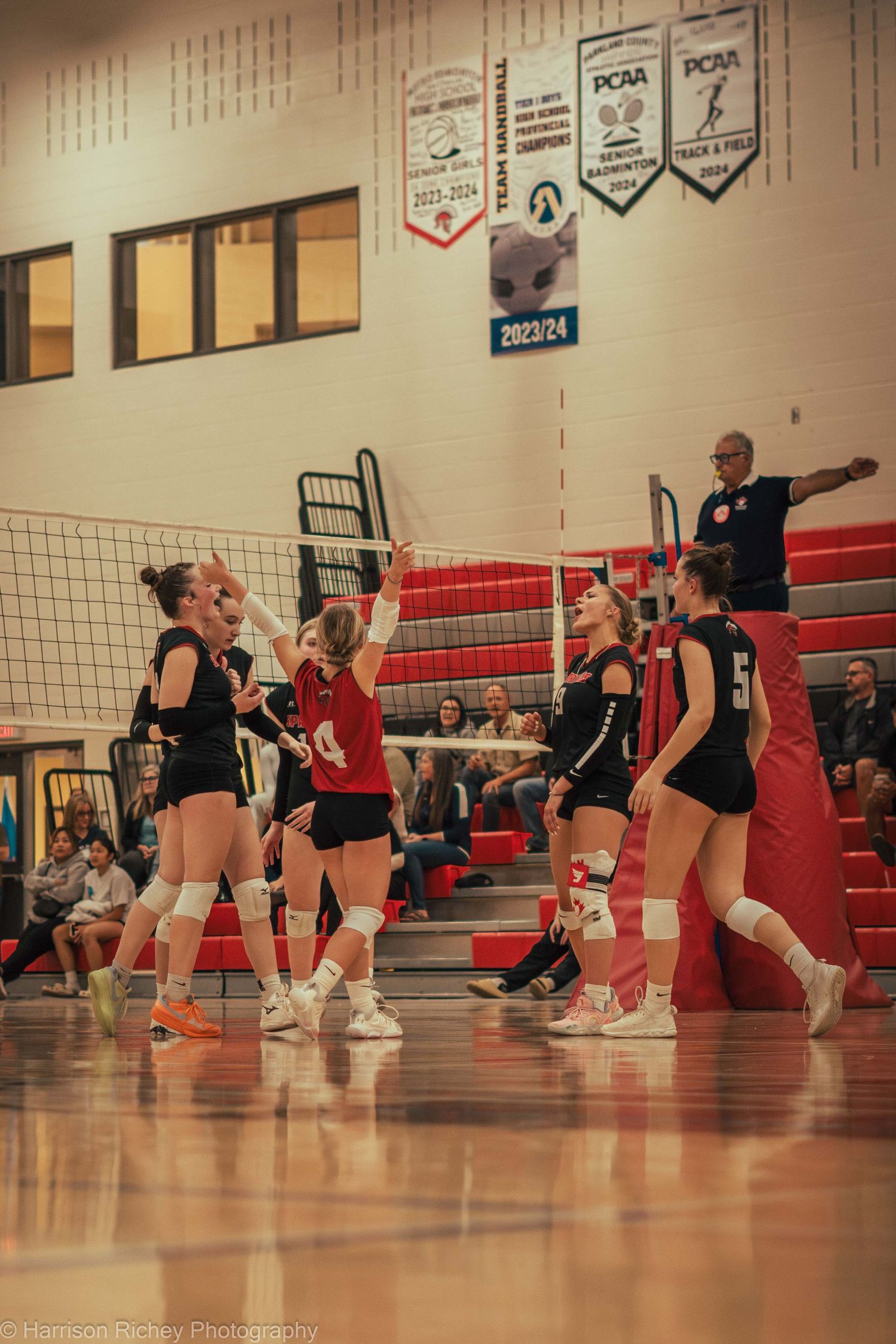 Volleyball players from opposing teams compete at the net during an intense indoor match.