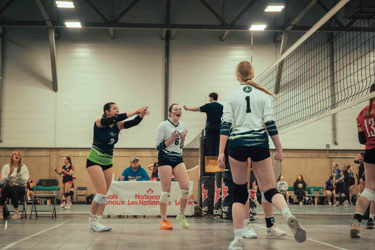 Indoor volleyball players compete at the net during an intense match in a gymnasium setting.