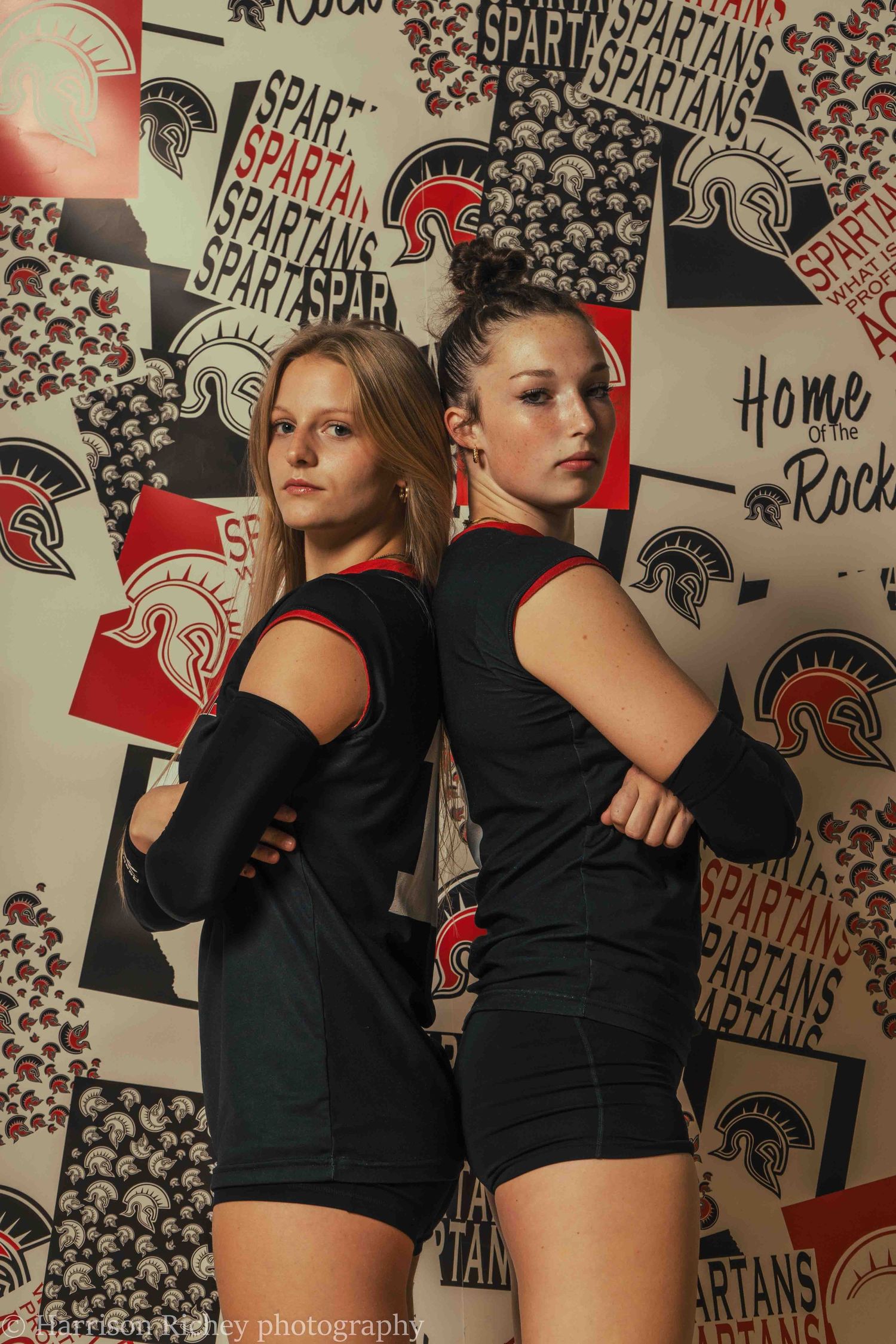 Athletes strike dramatic poses in black uniforms against a wall of Spartan team logos.