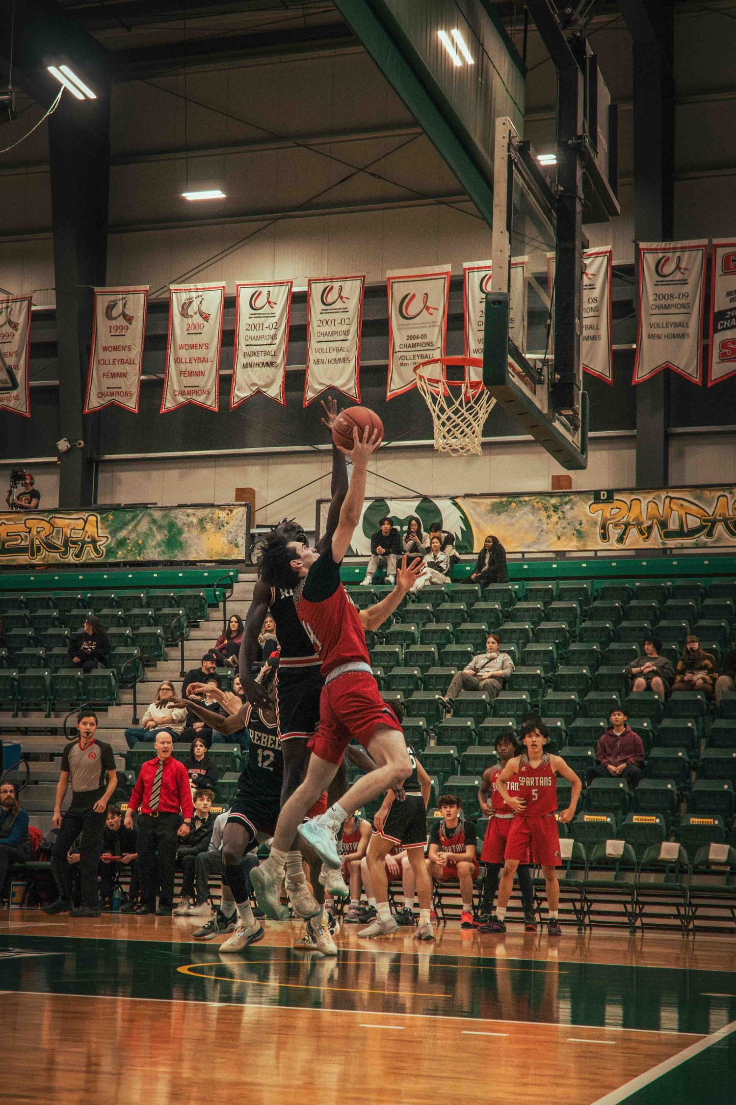 Players leap for a rebound under the basket during intense basketball game action.