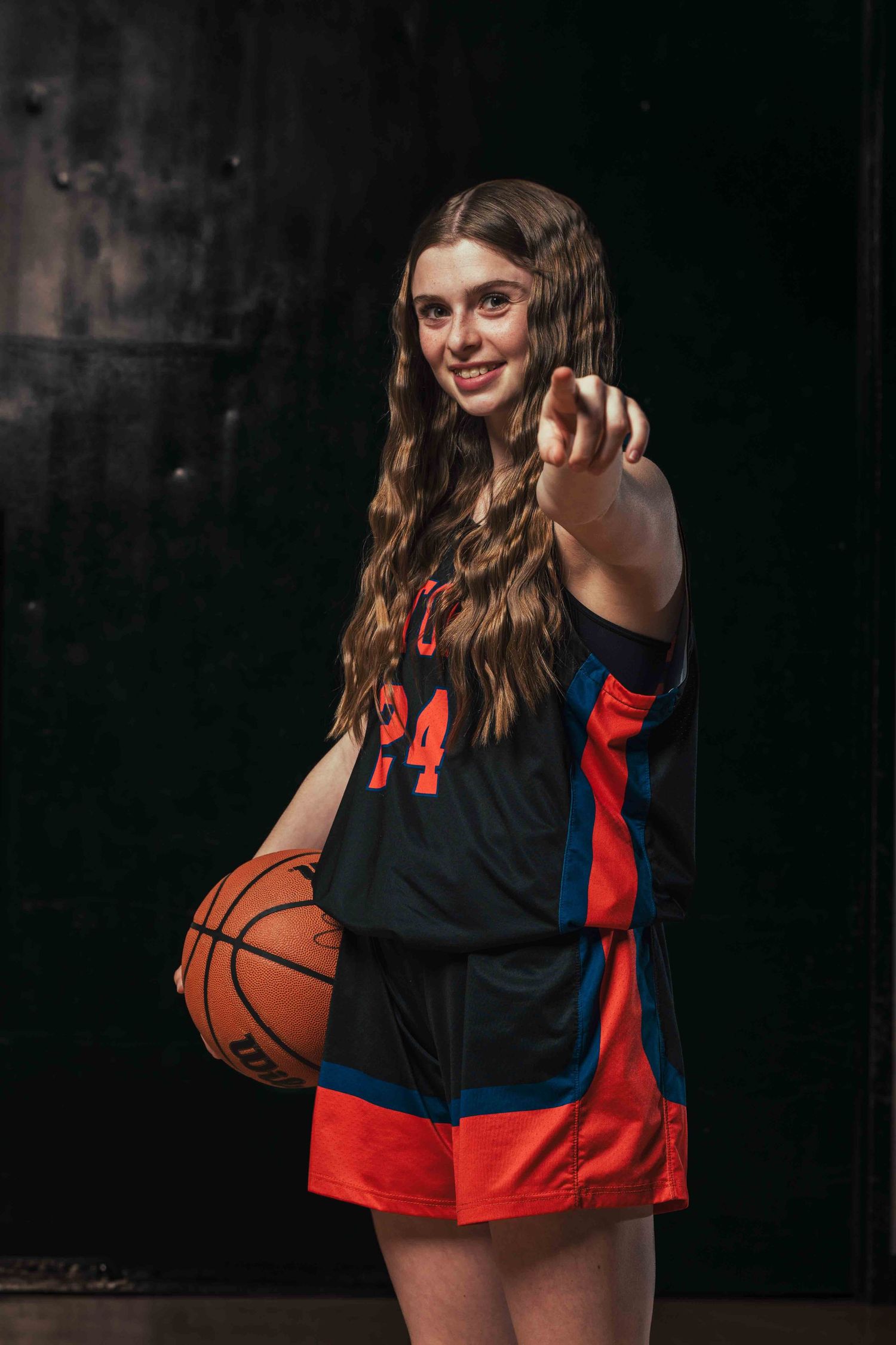 Basketball player in black and red uniform poses dynamically with ball against dark background.