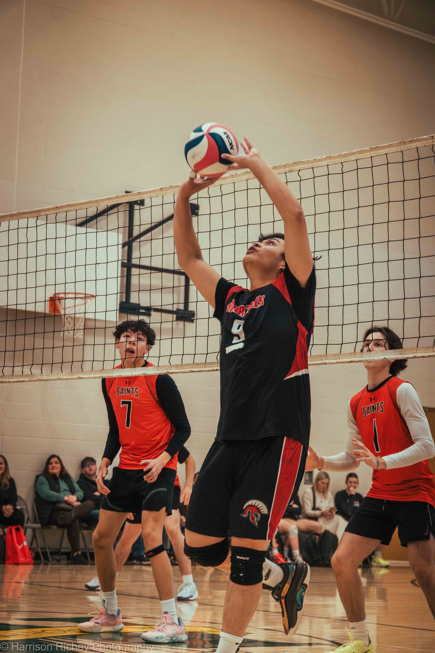 Players jump to hit a volleyball during an intense indoor game with a net between opposing teams.