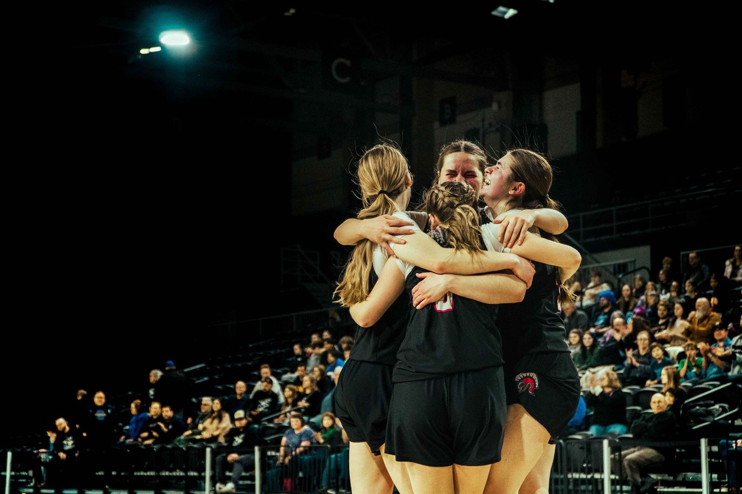 Team members embrace in celebration on the basketball court during a night game.