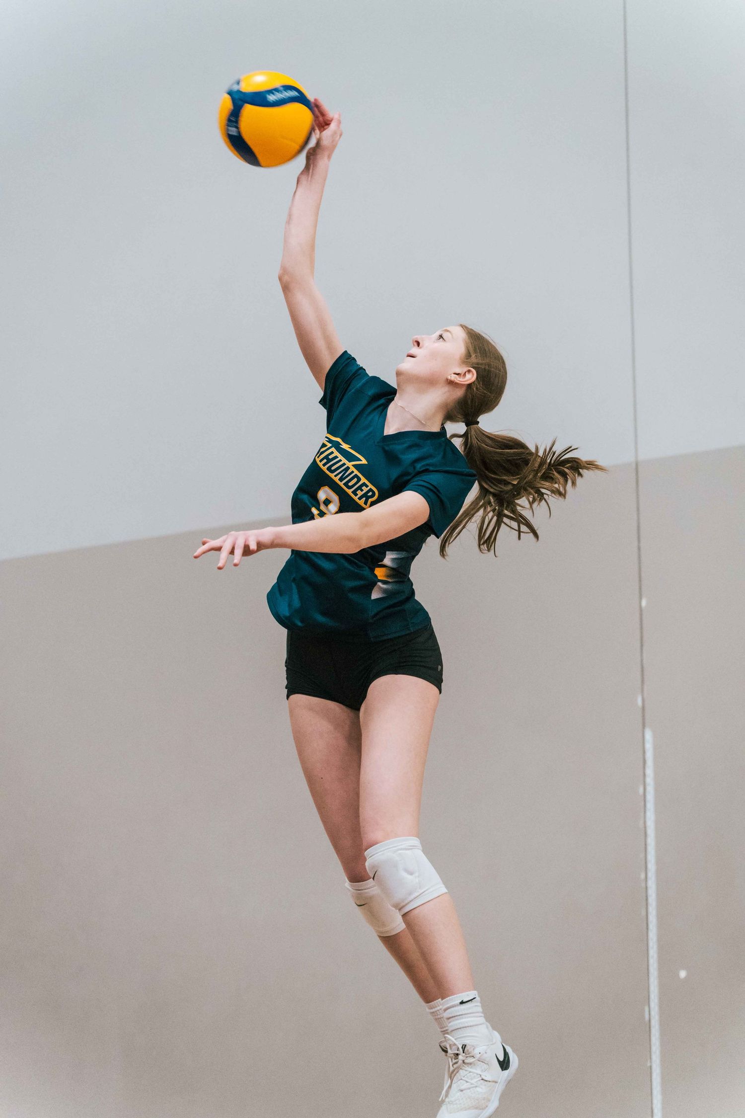 Volleyball player serves ball during practice session against plain wall.