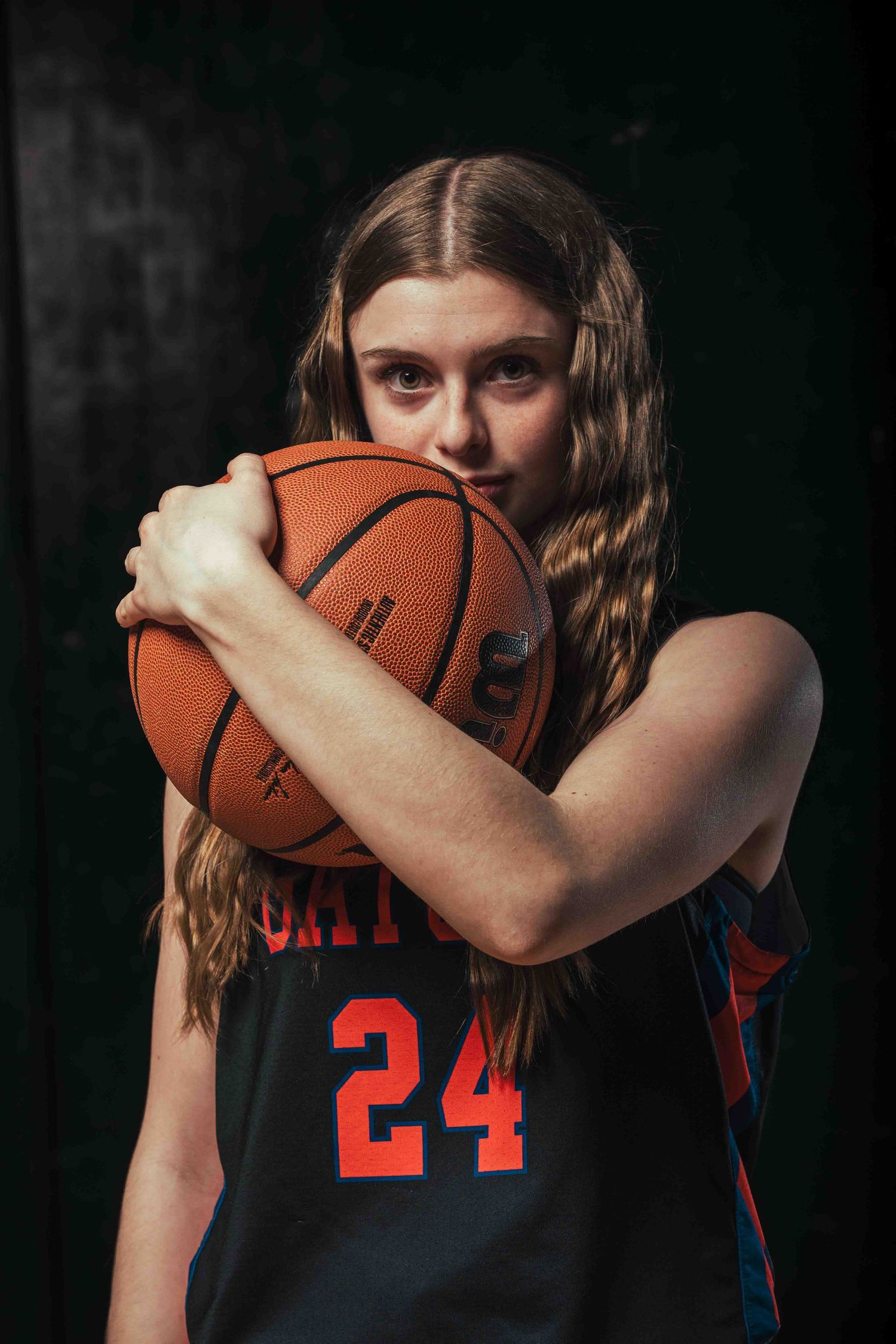 Basketball player in dark uniform holds ball close in dramatic portrait series.